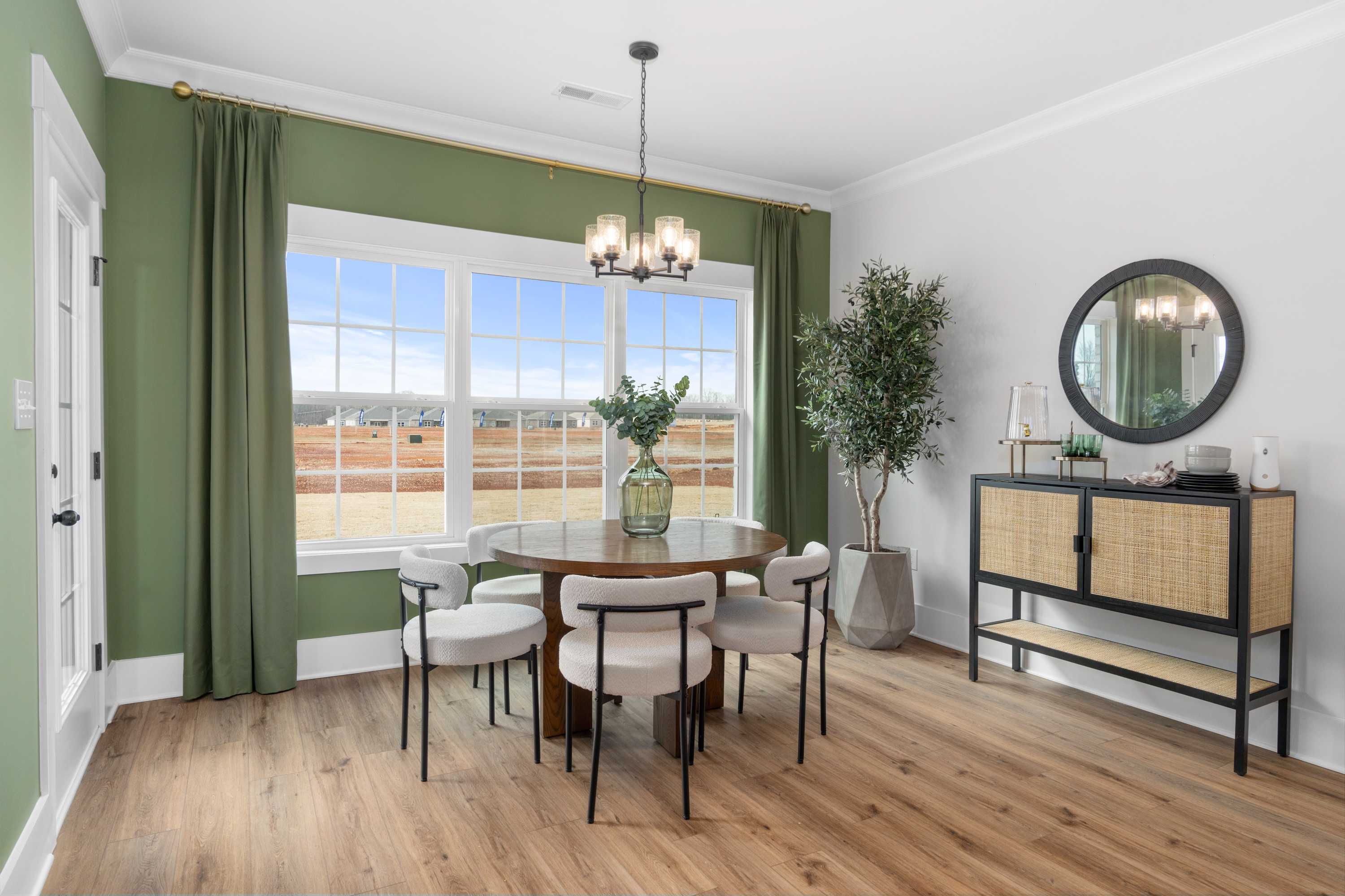 Spacious dining room in Briercreek Meridianville Alabama by Davidson Homes featuring round wooden table, upholstered chairs, green accent wall, chandelier, and hardwood floors