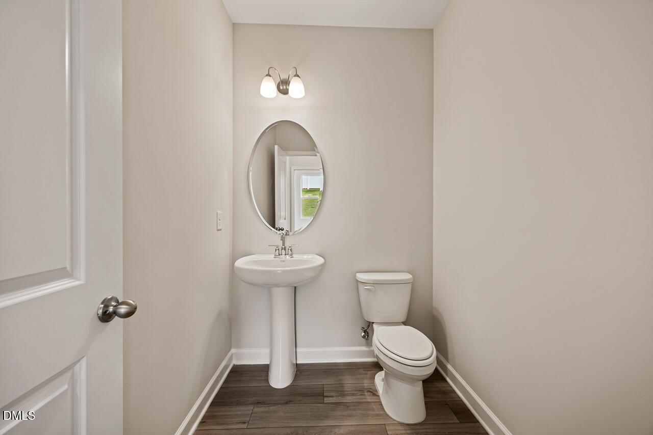 Half bathroom with pedestal sink and oval mirror in The Ash C floor plan at Woodland Crossing, Zebulon, North Carolina.