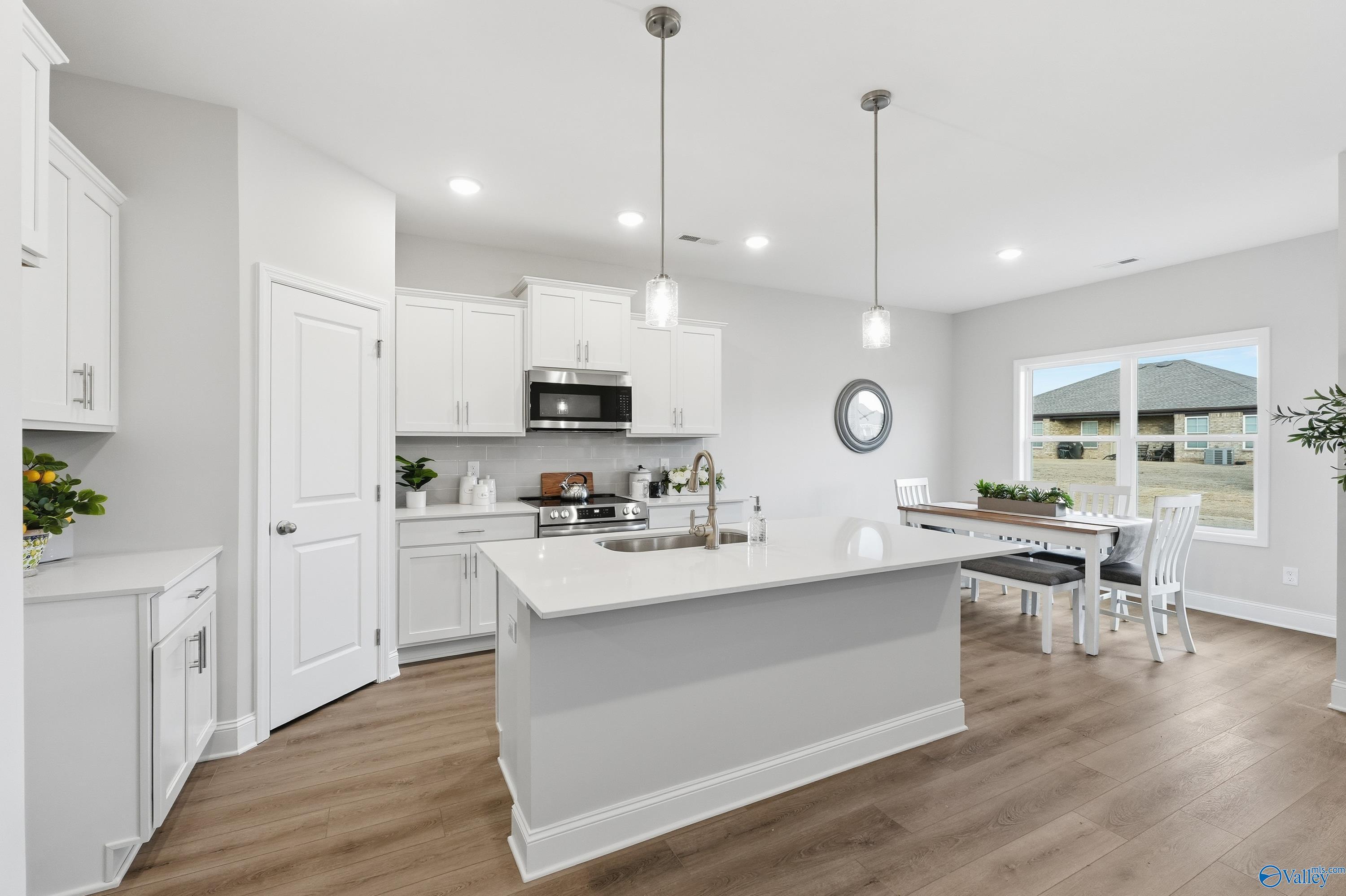 Modern white kitchen with central island sink, cabinetry, and dining area overlooking yard in Davidson Homes The Asheville, Toney, AL