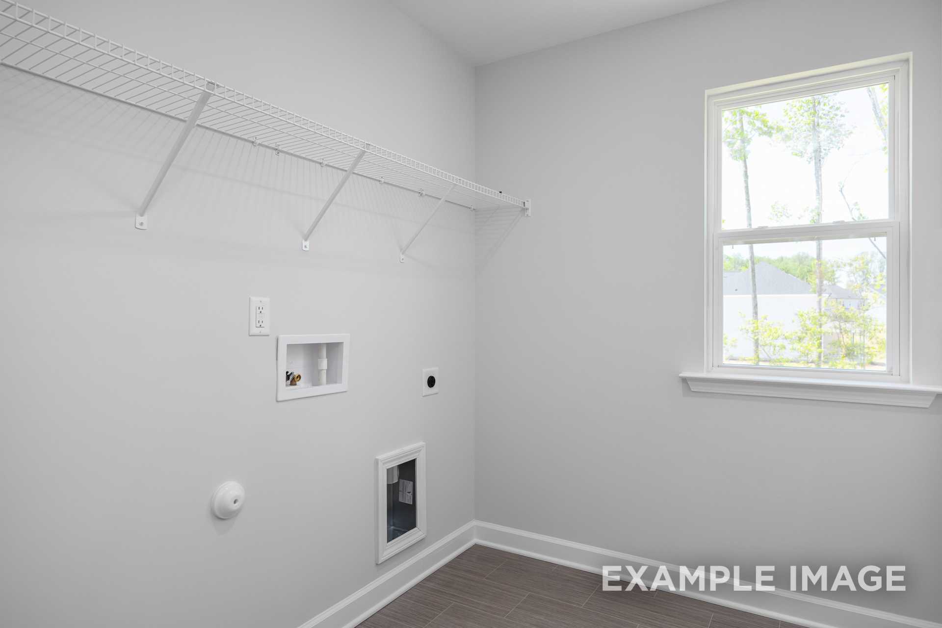 Spacious laundry room in The Gavin C featuring white wire shelving, large window, utility sink, outlets, and pet door on wood floor
