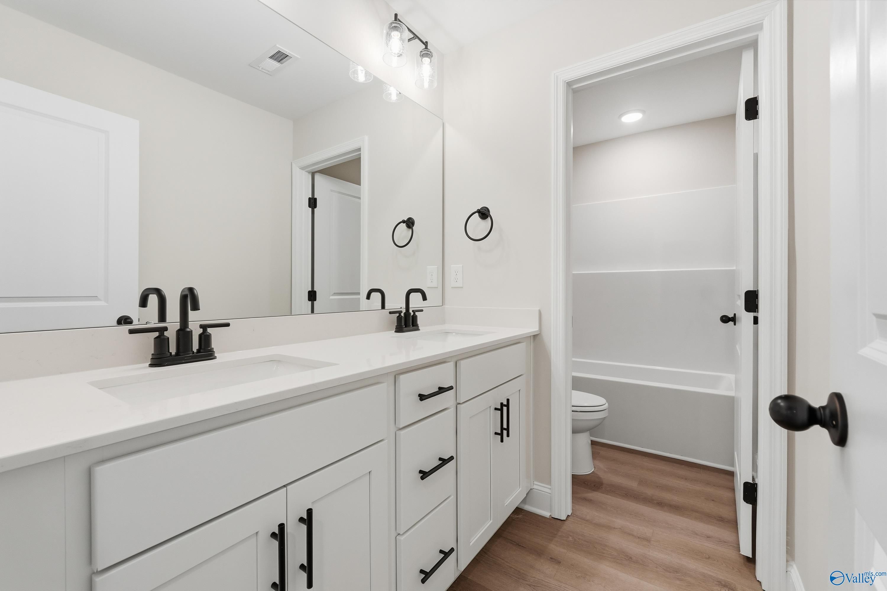 Elegant master bathroom with double white quartz vanity, black fixtures, and adjacent tub in Davidson Homes The Chelsea C, Harvest, Alabama