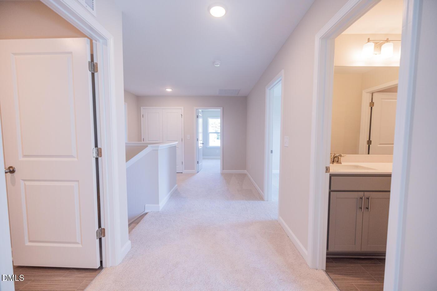Bright upstairs hallway with carpeted flooring, open bedroom doors, and modern bathroom vanity in The Hickory II C, Zebulon, NC