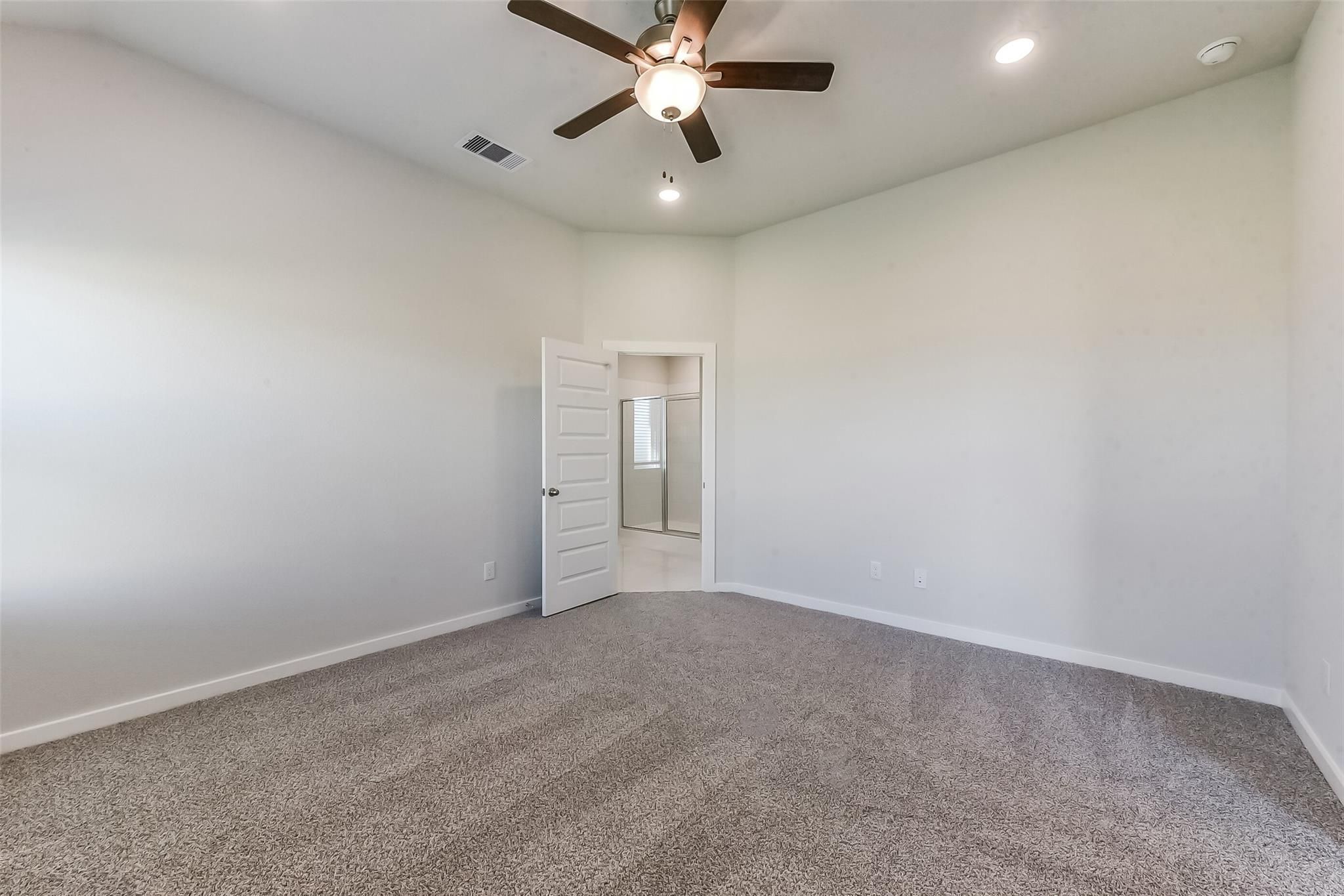 Spacious master bedroom with beige carpet, ceiling fan, and open en-suite bath door in Davidson Homes The Costa B, Dayton, Texas