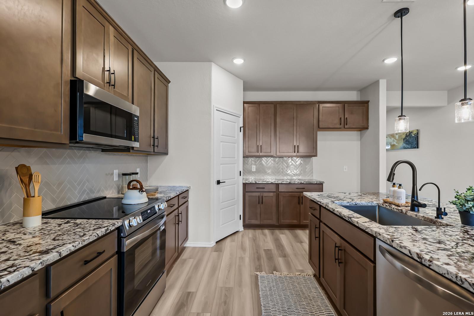 Modern kitchen with granite countertops, stainless appliances, and wood cabinets in The Douglas C floor plan, Seguin, TX.