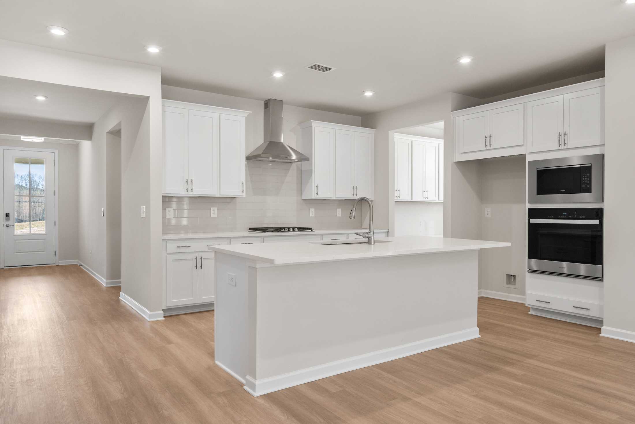 The Dawson C modern kitchen with white shaker cabinets, large quartz island, stainless steel double oven, and open hardwood floors