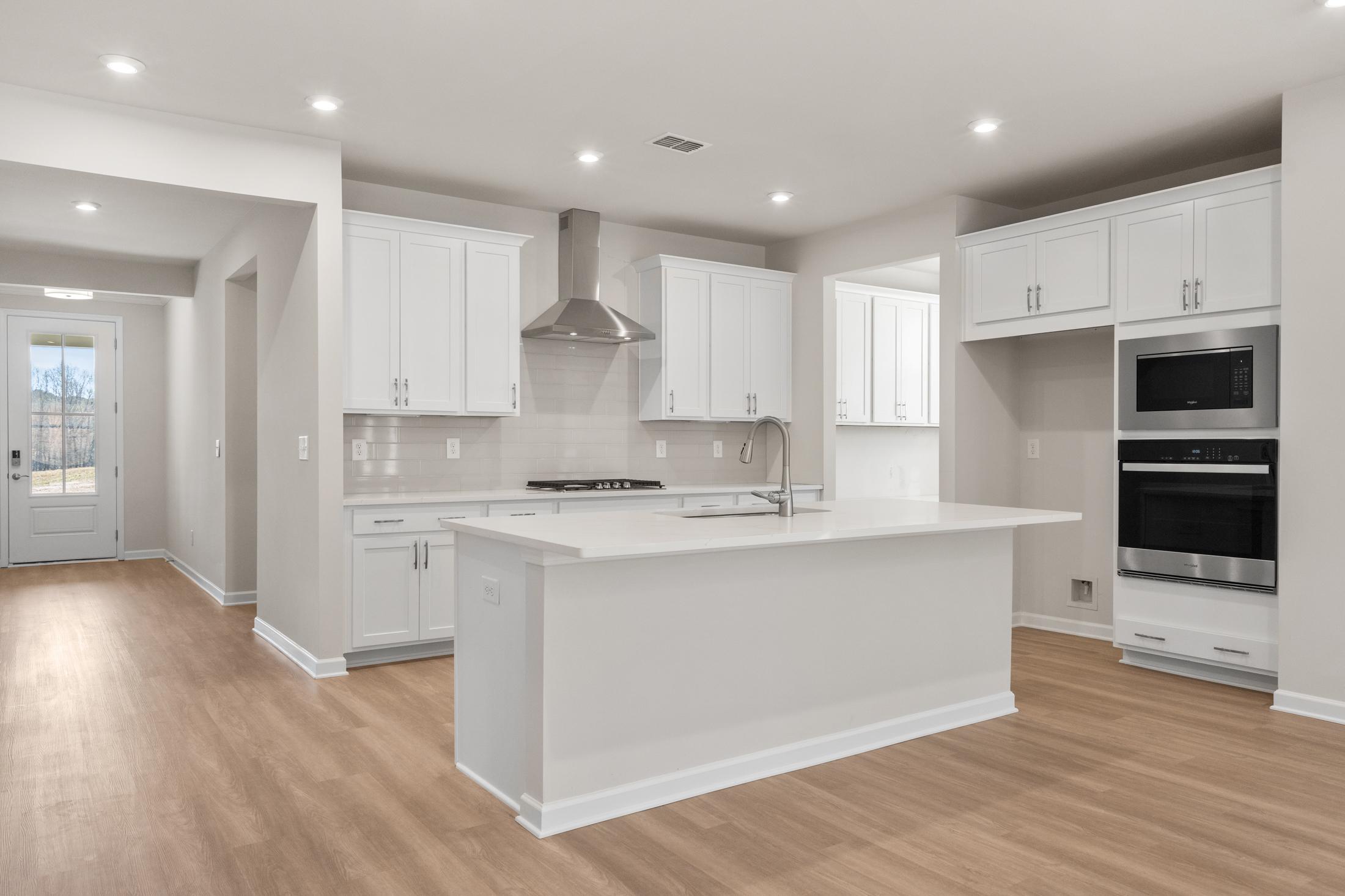 The Dawson C modern kitchen with white shaker cabinets, large quartz island, stainless steel double oven, and open hardwood floors