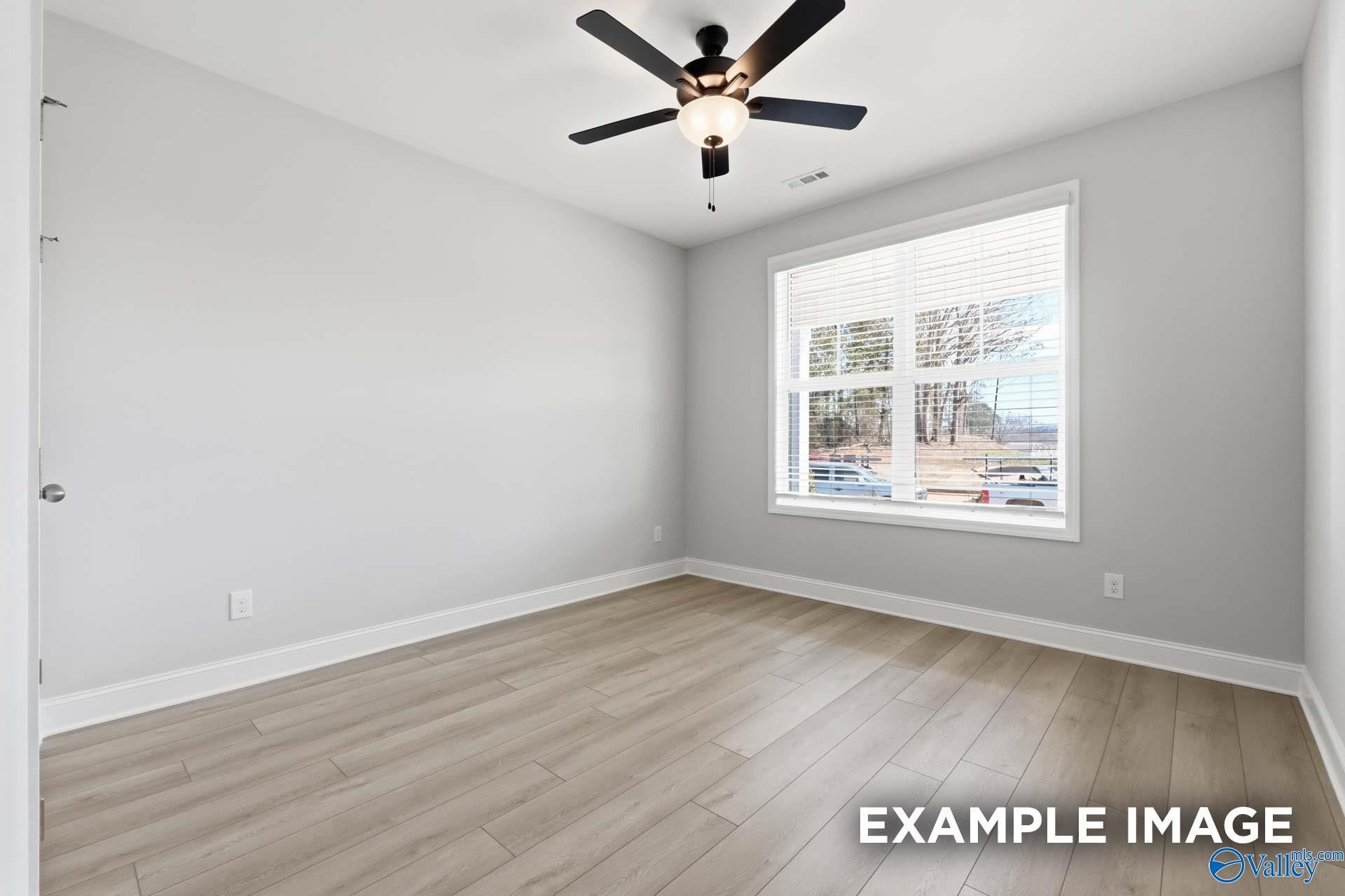 Bright empty bedroom with ceiling fan, gray walls, hardwood floors, and window view in The Harrison C, Madison, Alabama