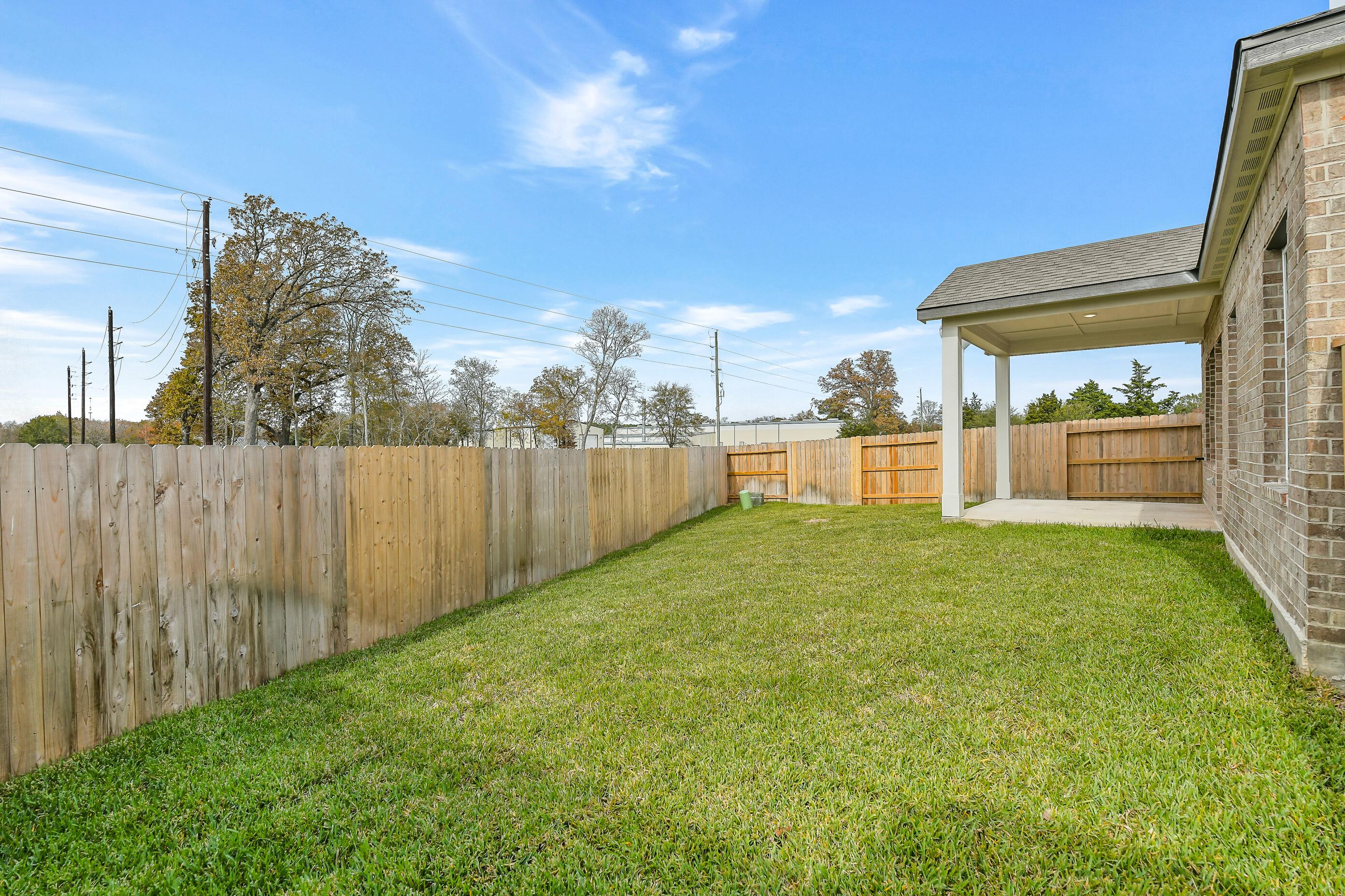 Private fenced backyard with lush green lawn, covered patio, and brick home in Davidson Homes The Colorado G, Windmill Estates, Magnolia Texas