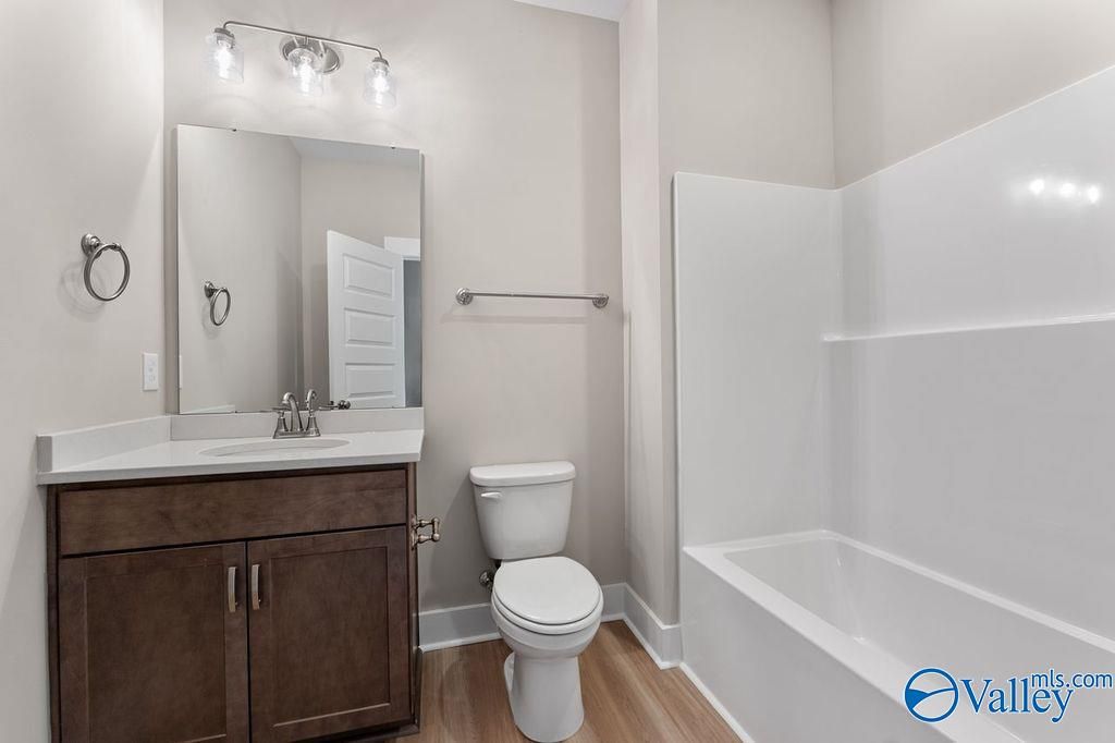 Elegant secondary bathroom with wood vanity, soaking tub, walk-in shower, and soft lighting in Evermore Homes The Oxford, Owens Cross Roads, AL