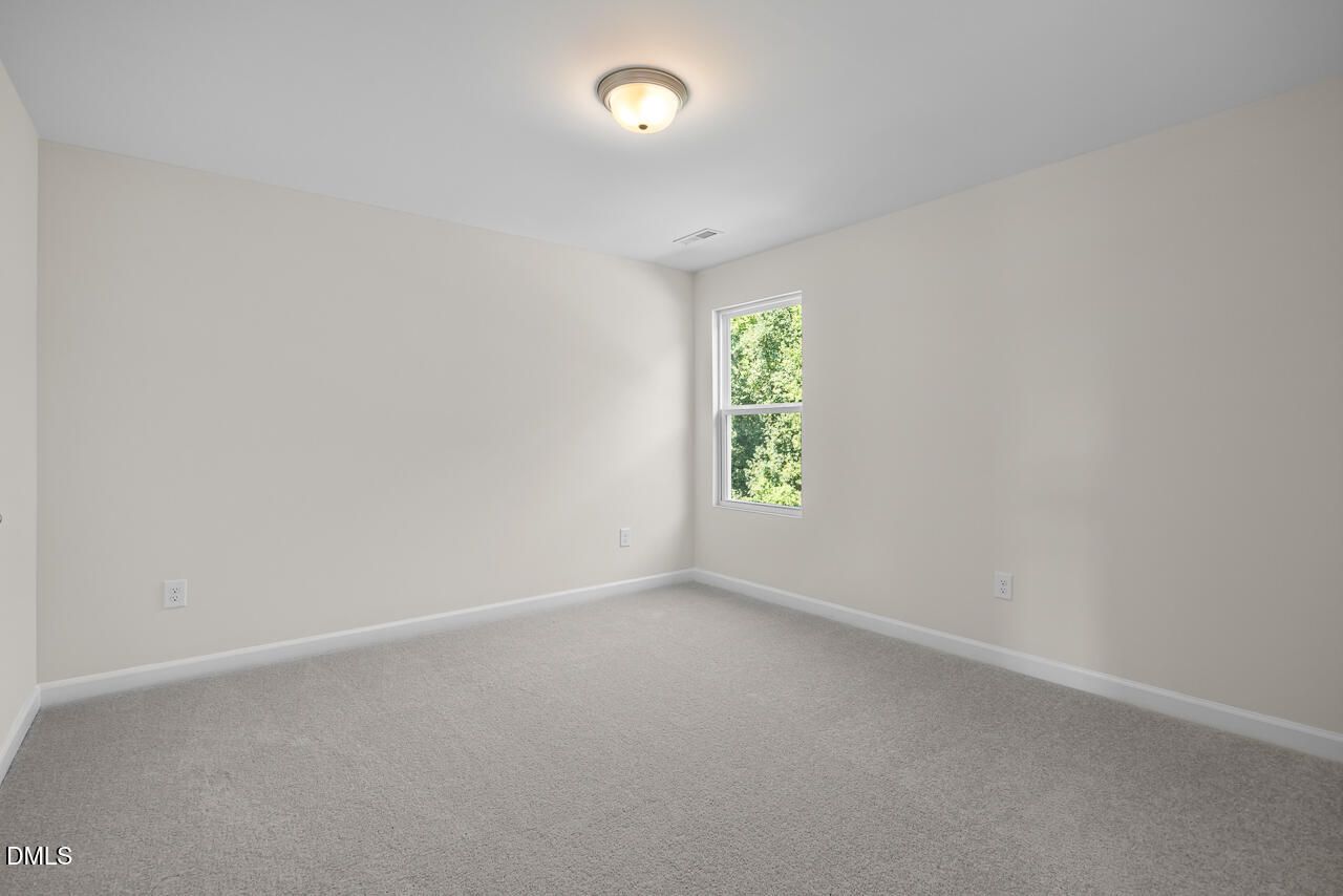 Bright empty bedroom with neutral walls, carpet, and window overlooking trees in Davidson Homes Willow C, Zebulon NC
