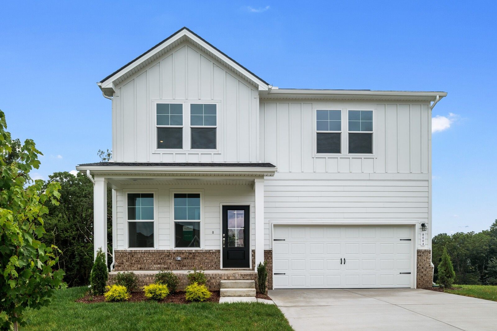 Two-story white farmhouse exterior with brick accents and a 2-car garage in Calista Farms, White House, Tennessee.
