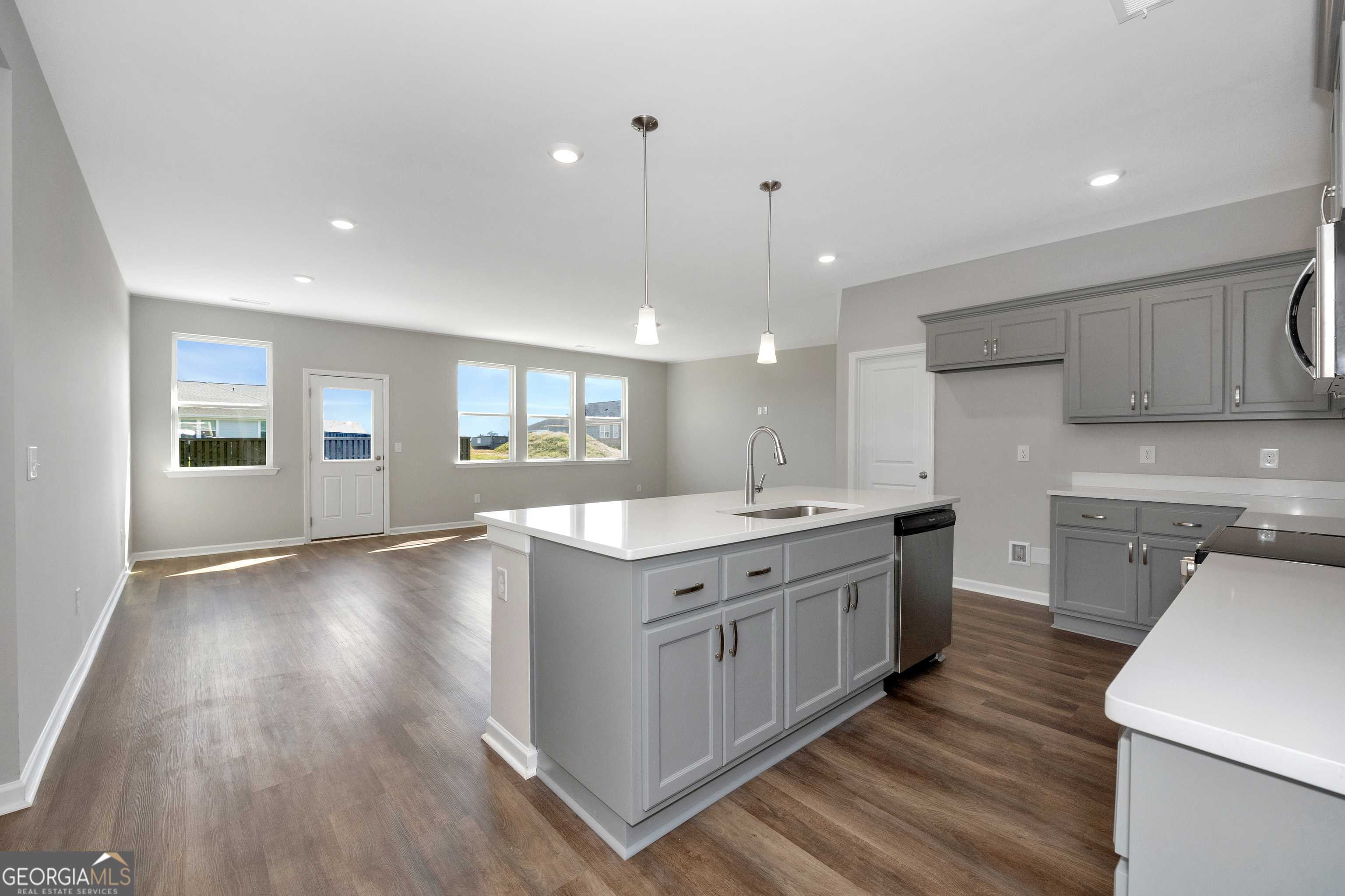 Modern open-concept kitchen with gray shaker cabinets, white quartz island sink, and large windows in Evermore Homes The Luna, Perry, GA