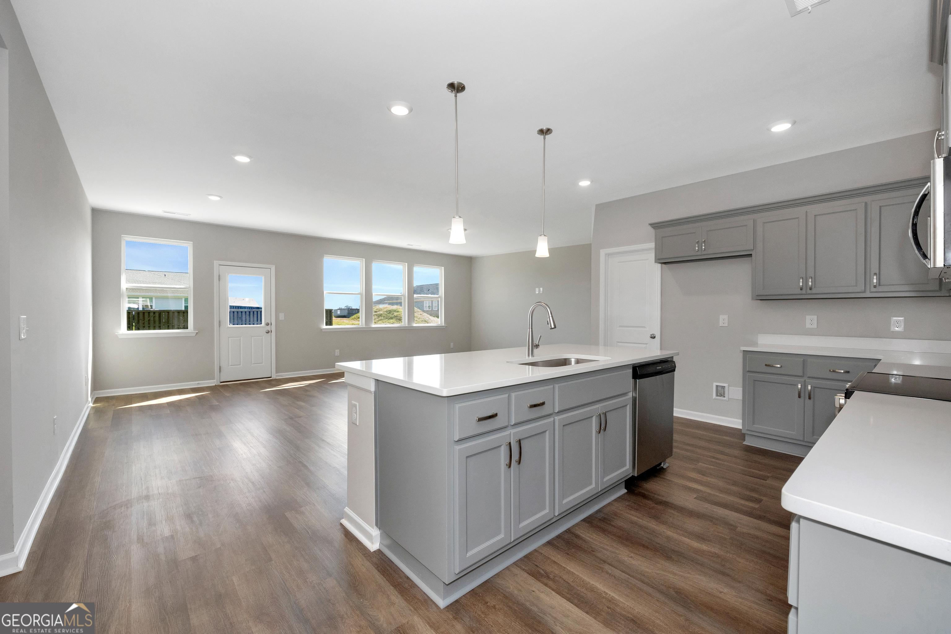 Modern open-concept kitchen featuring gray shaker cabinets, white quartz island, stainless sink, and large windows in Evermore Homes The Luna, Perry, GA