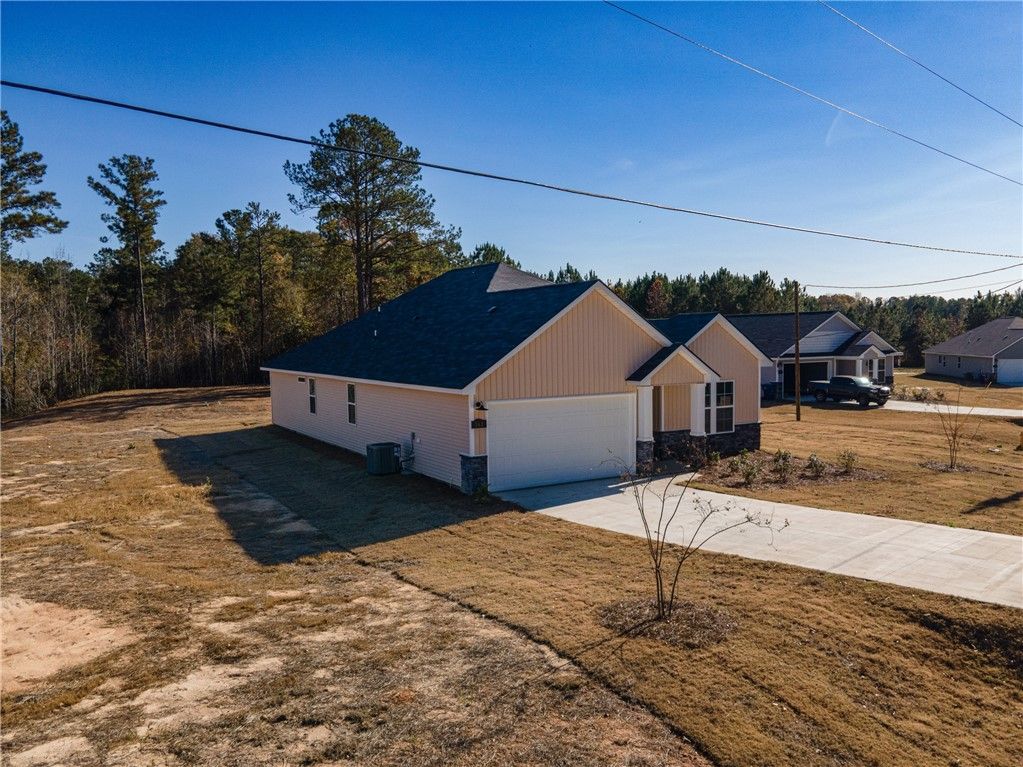 Side view of single-story beige home with one-car garage and dark roof amid pine trees in Silver Oak, Cusseta, Alabama - Evermore The Orion