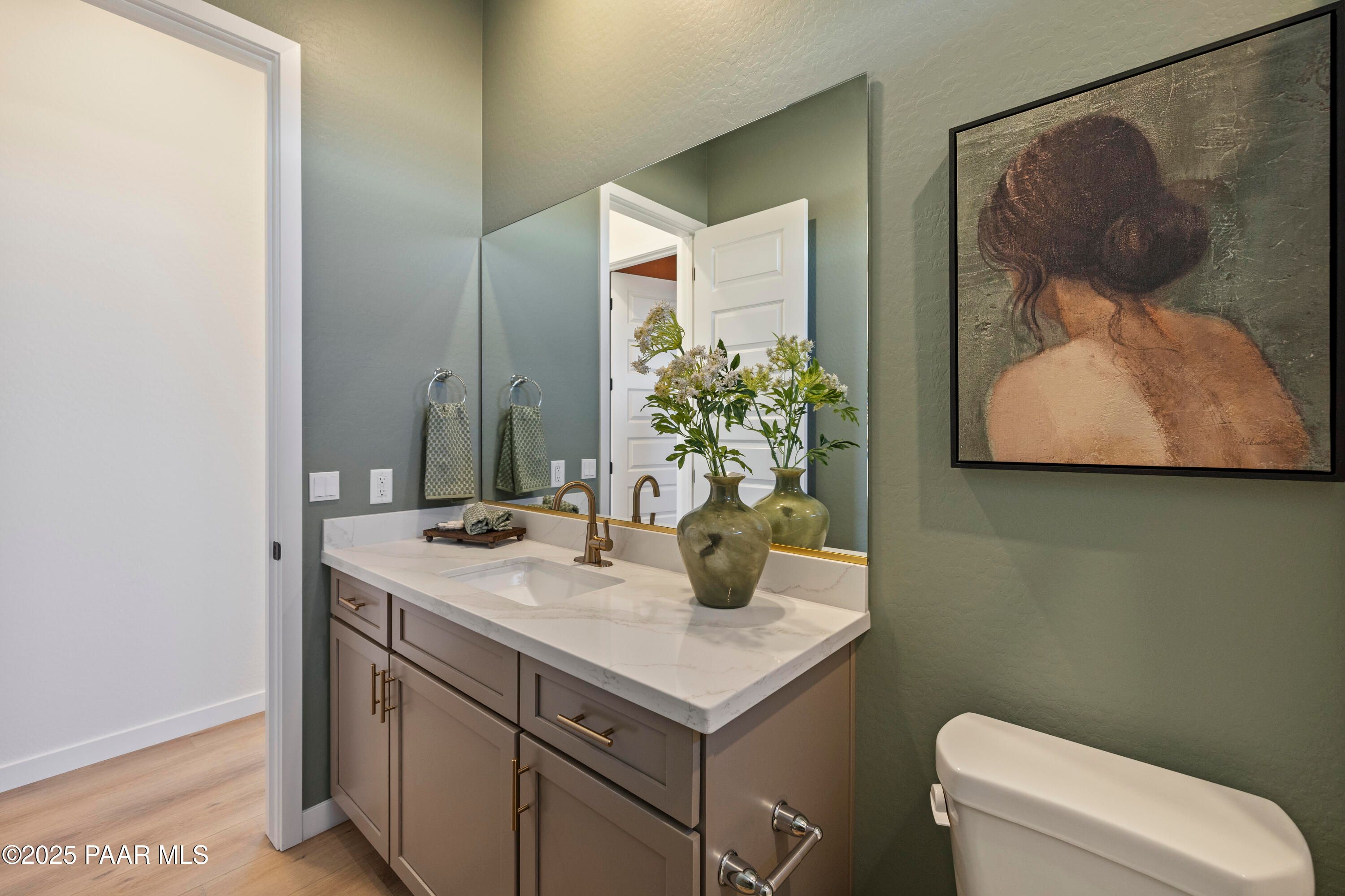 Elegant powder room with double vanity, quartz countertop, green walls, and floral vase in Davidson Homes The Blaze D, Prescott, AZ