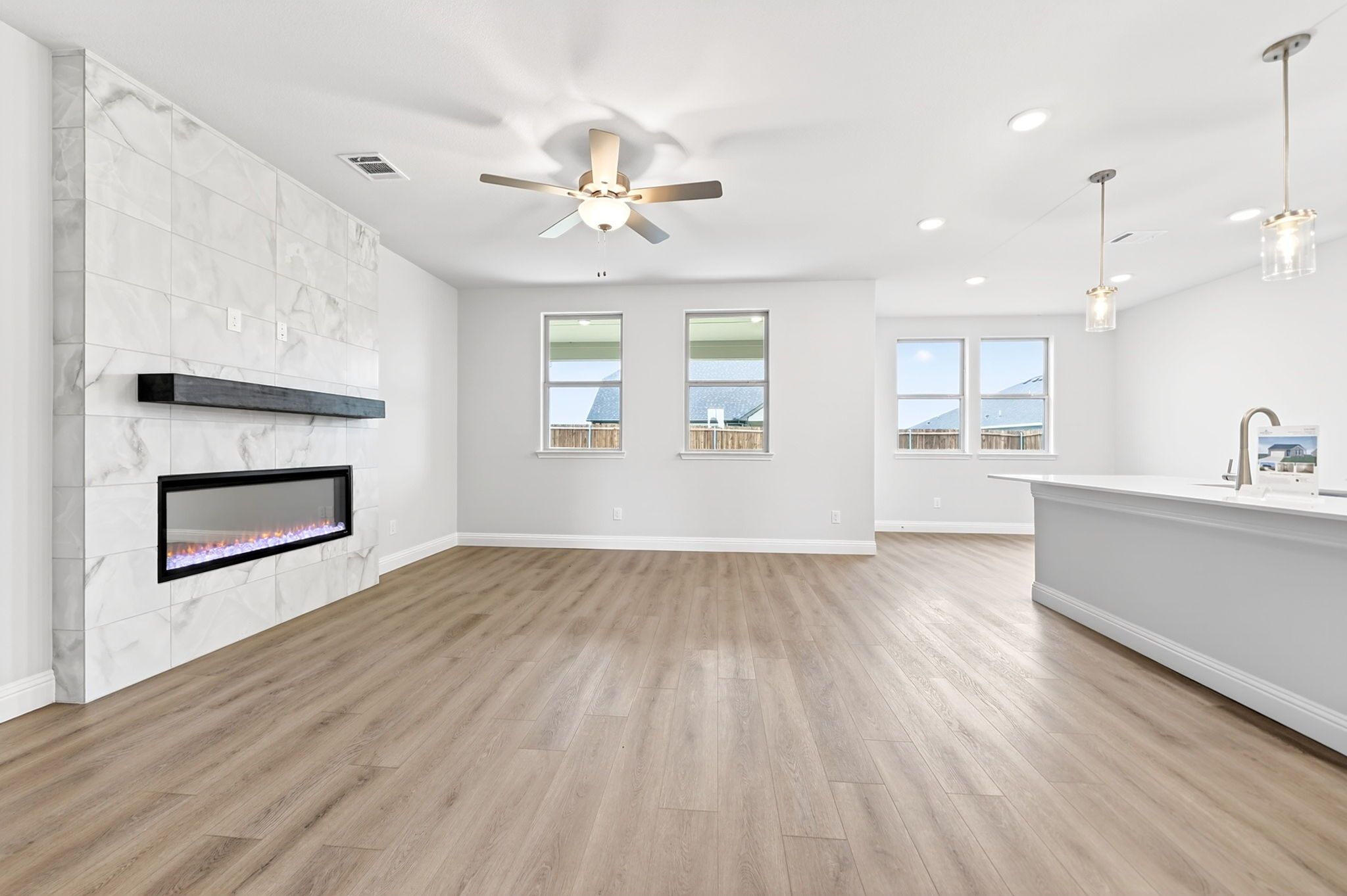 Open-concept living room in The Redbud design featuring a marble-tiled fireplace and modern kitchen island.
