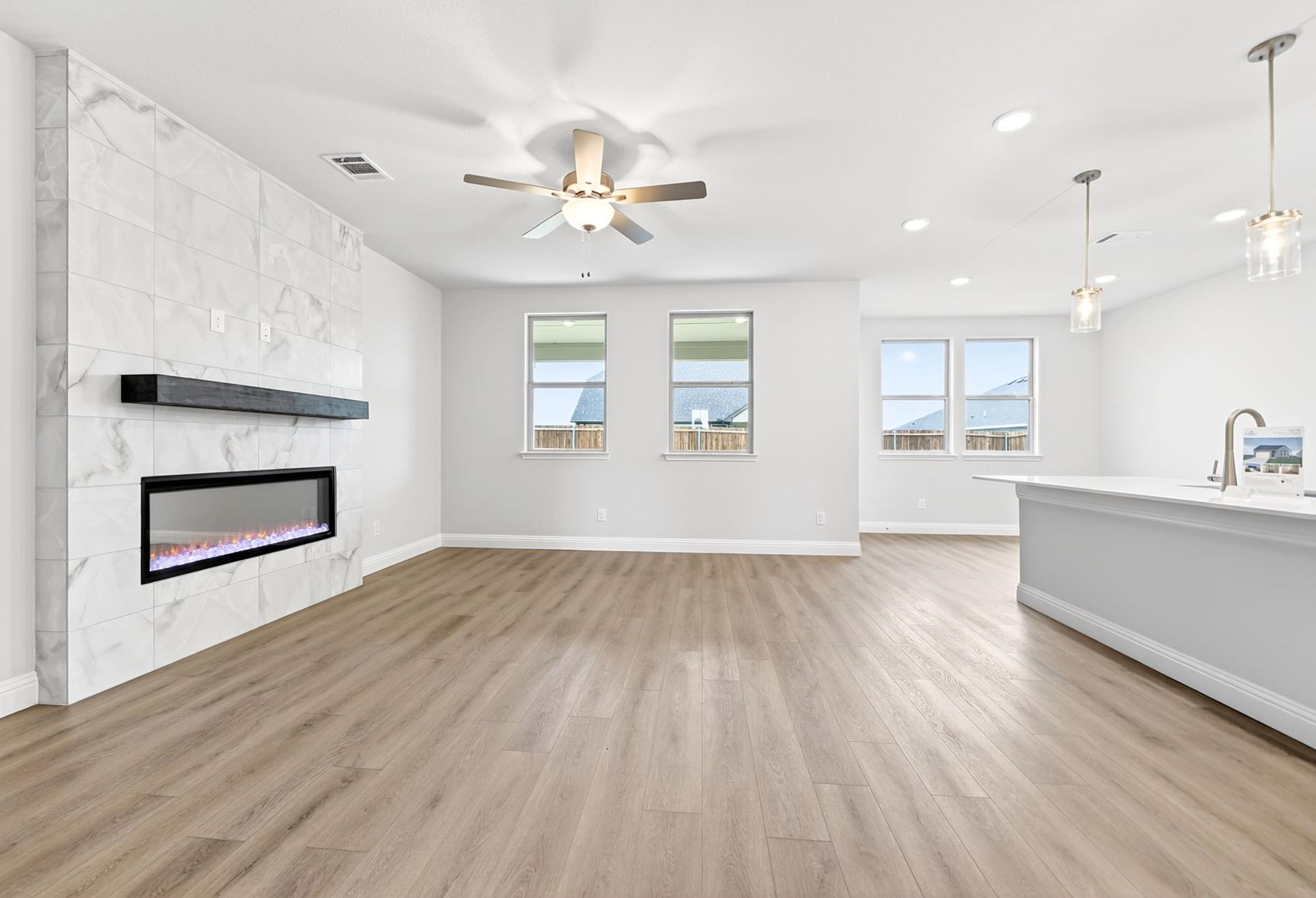 Open-concept living room in The Redbud design featuring a marble-tiled fireplace and modern kitchen island.