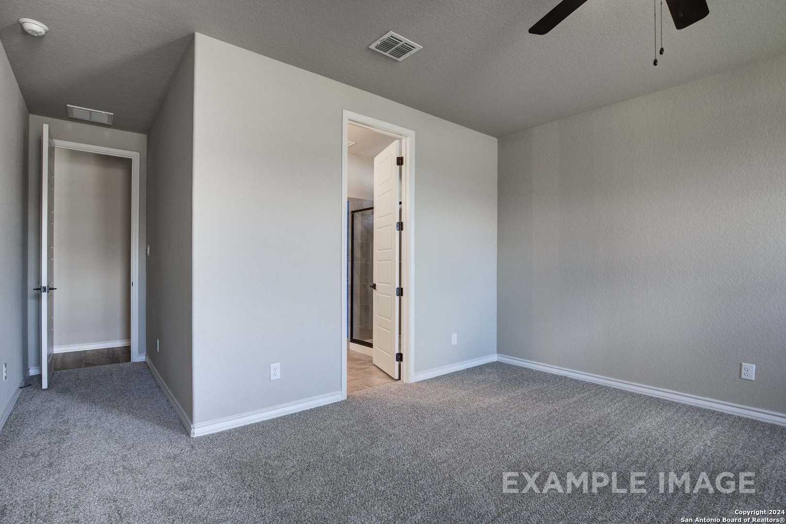 Spacious master bedroom with ceiling fan, gray carpet, and en-suite bath door in Davidson Homes The Rockford G, Ladera, San Antonio