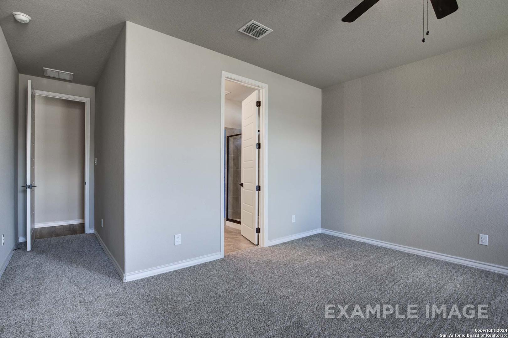 Spacious master bedroom with ceiling fan, gray carpet, and en-suite bath door in Davidson Homes The Rockford G, Ladera, San Antonio