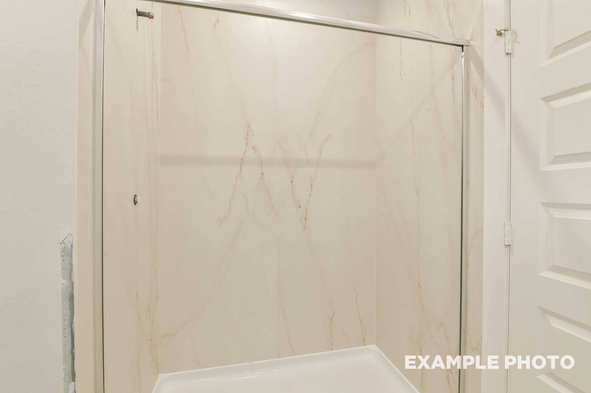 Marble-look shower surround with sliding glass door in bathroom of The Colorado by Davidson Homes, Beasley, TX