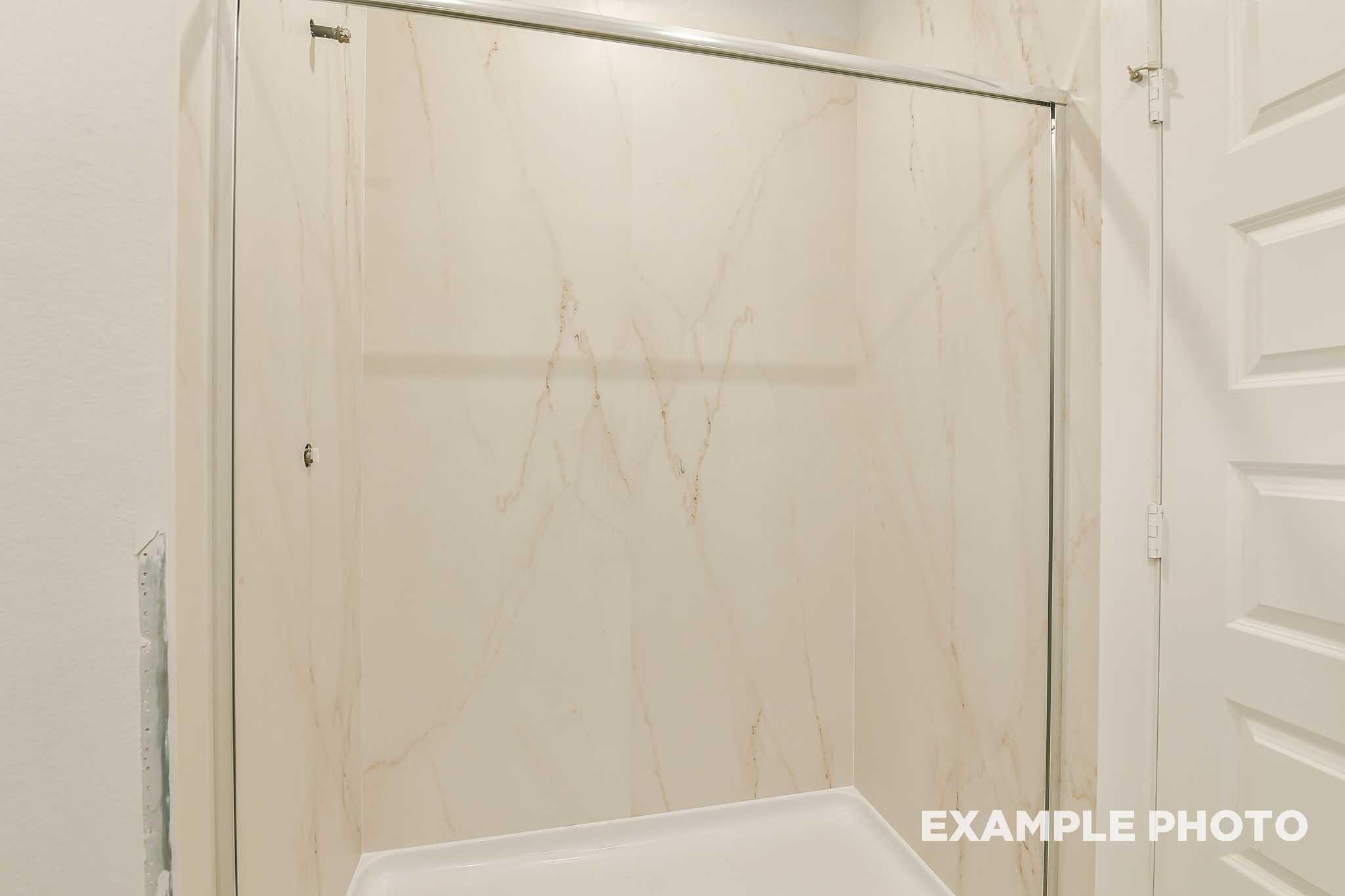Marble-look shower surround with sliding glass door in bathroom of The Colorado by Davidson Homes, Beasley, TX