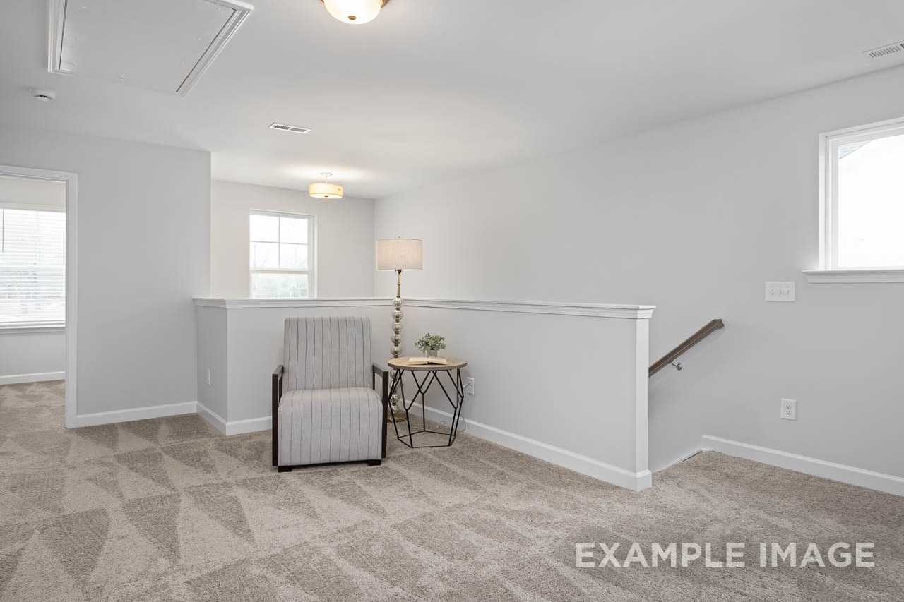 Upstairs loft seating in The Grace A 2-story home featuring striped armchair, plant table, staircase railing, Davidson Homes Lillington NC