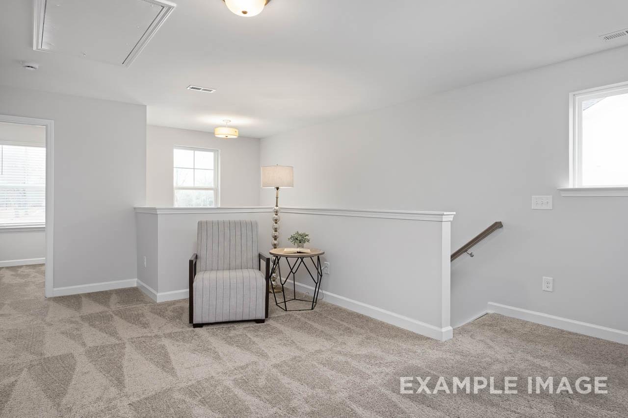 Upstairs loft seating in The Grace A 2-story home featuring striped armchair, plant table, staircase railing, Davidson Homes Lillington NC