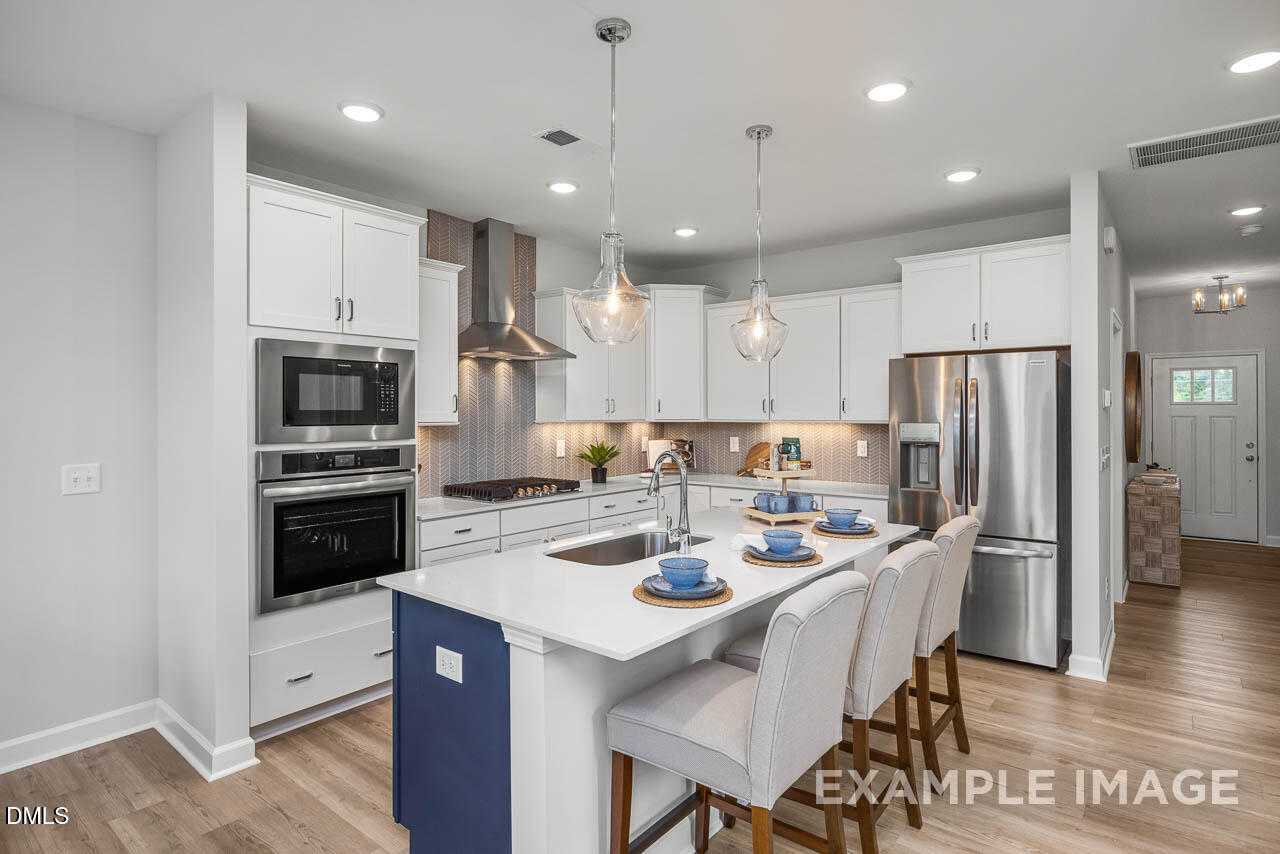 Modern white kitchen with island, stainless appliances, pendant lights in Davidson Homes The Graham, Fuquay-Varina, NC