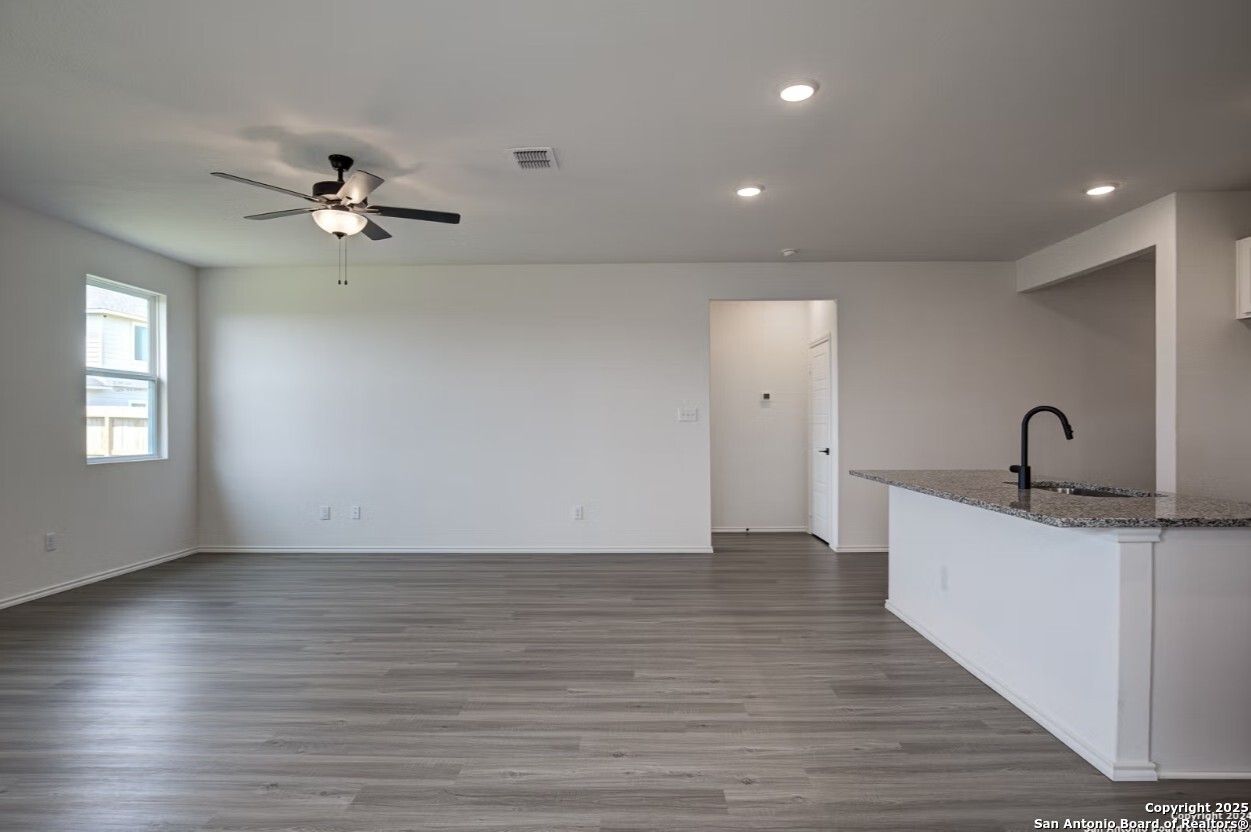 Open living area with ceiling fan, large windows, white kitchen island, and gray flooring in The Daphne H by Davidson Homes, Seguin, Texas