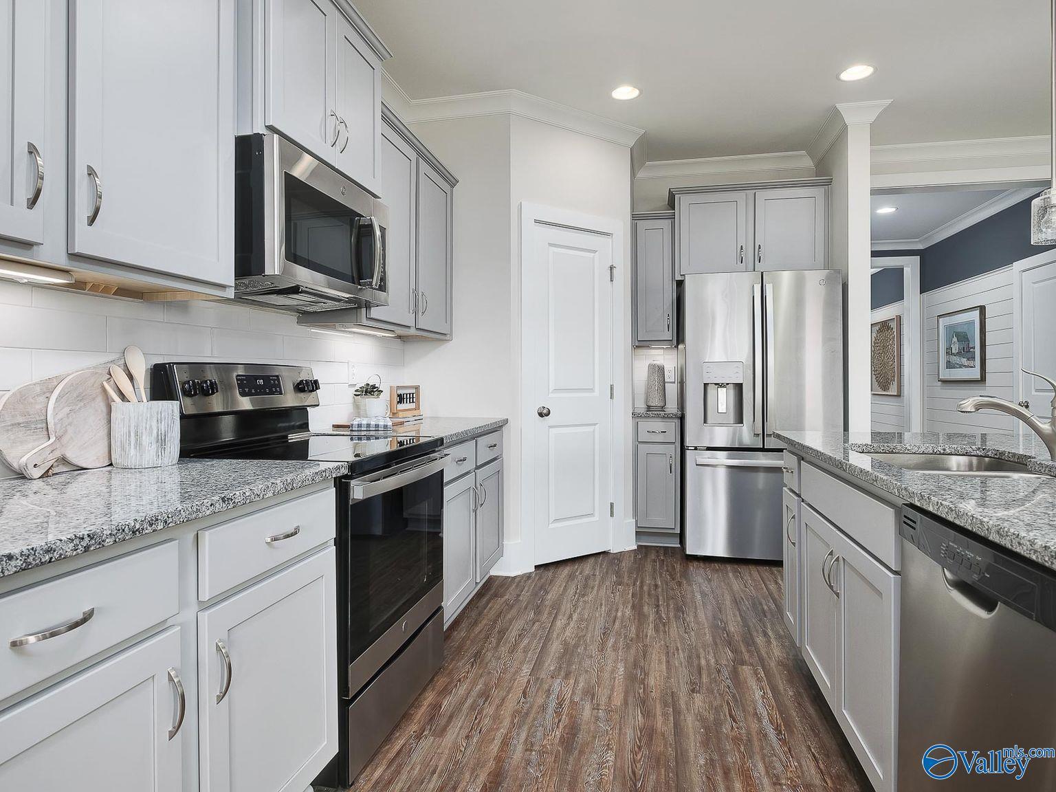 Modern white shaker kitchen with granite counters, stainless steel appliances, and large island in Davidson Homes The Everett, Toney AL