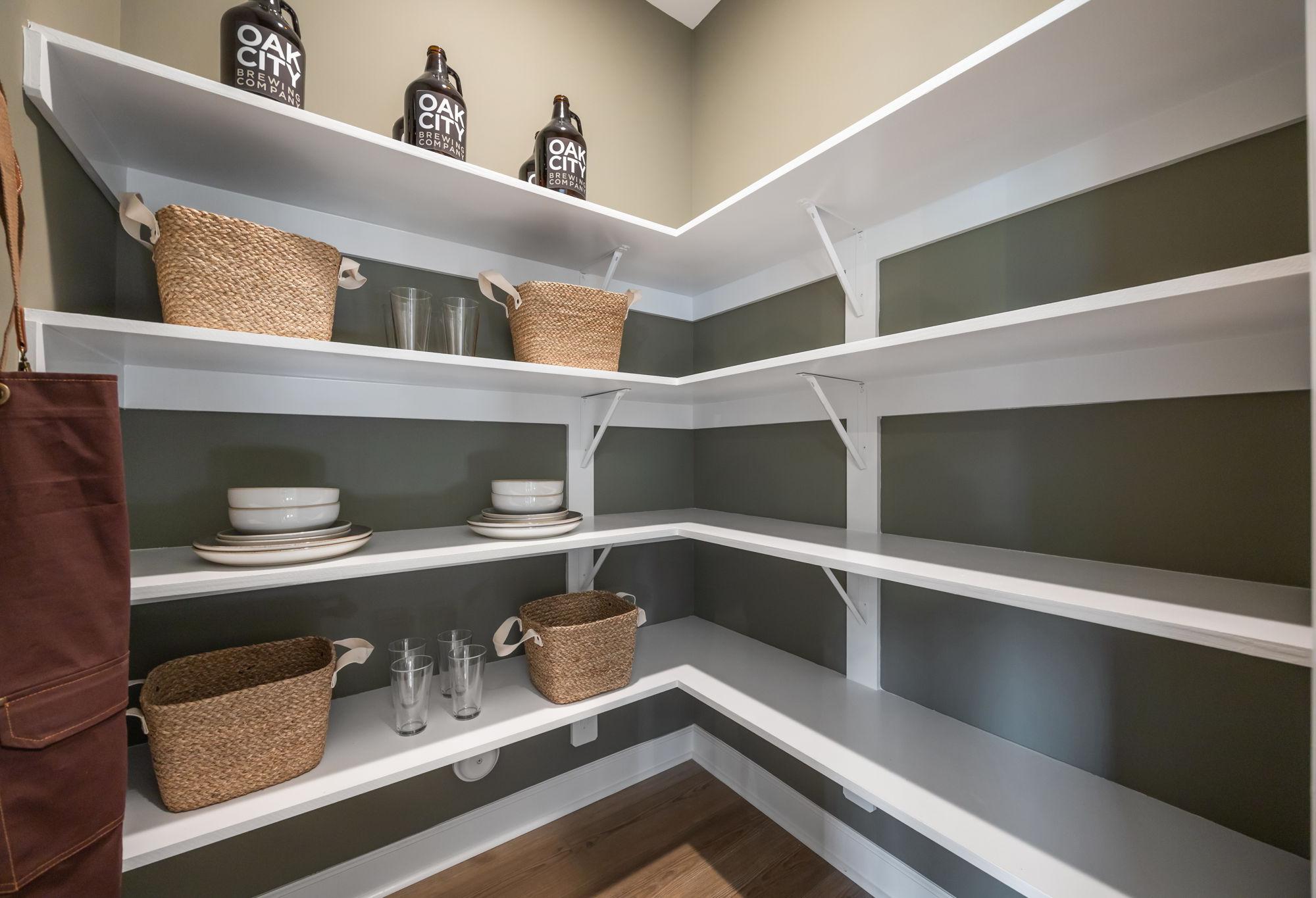Organized walk-in pantry in The Mitchell featuring white wrap-around shelving, storage baskets, and kitchen essentials.