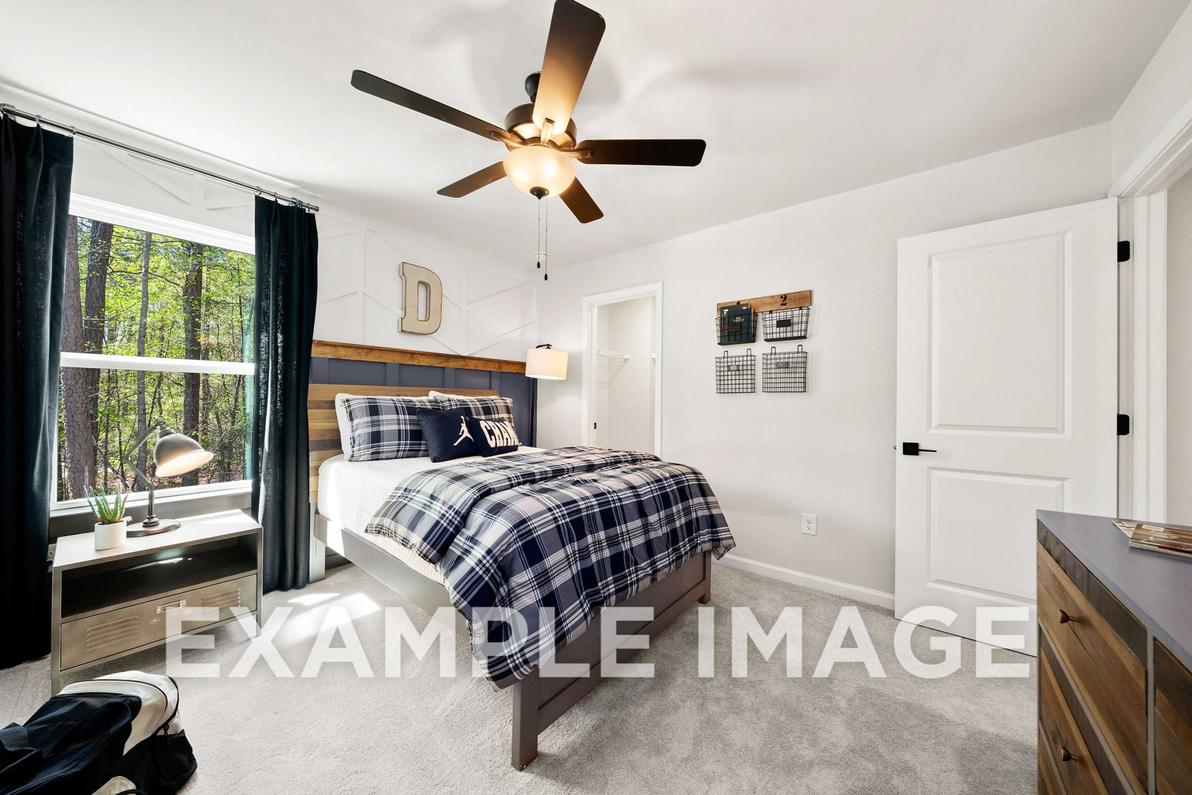 Spacious upper-floor bedroom in The Hickory A featuring plaid bedding, wooden headboard, ceiling fan, dresser, and tree-view window