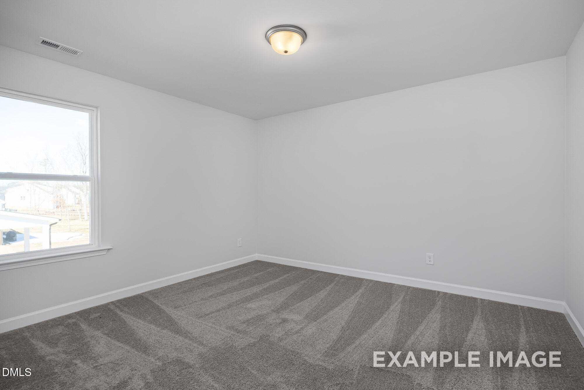 Bright empty bedroom with white walls, large window, ceiling light, and gray carpet in Davidson Homes The Cypress B II, Angier, NC