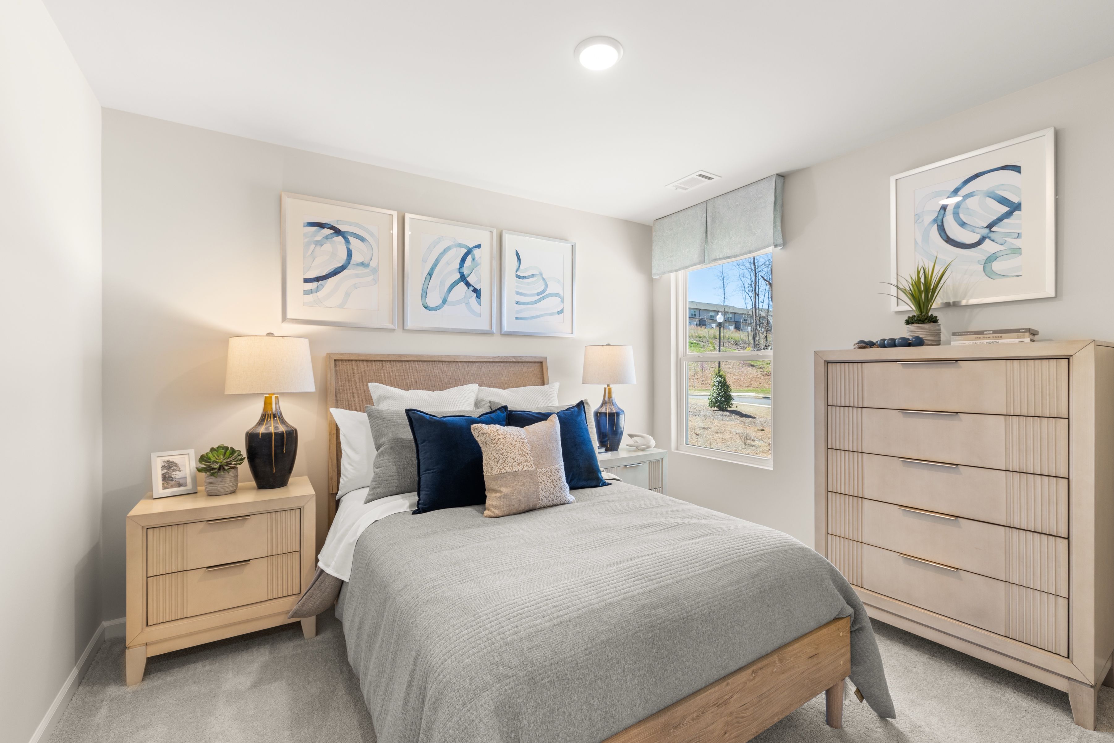 Cozy bedroom at The Bluffs in Canton, Georgia by Davidson Homes featuring gray queen bed, blue accents, wooden furniture, abstract art