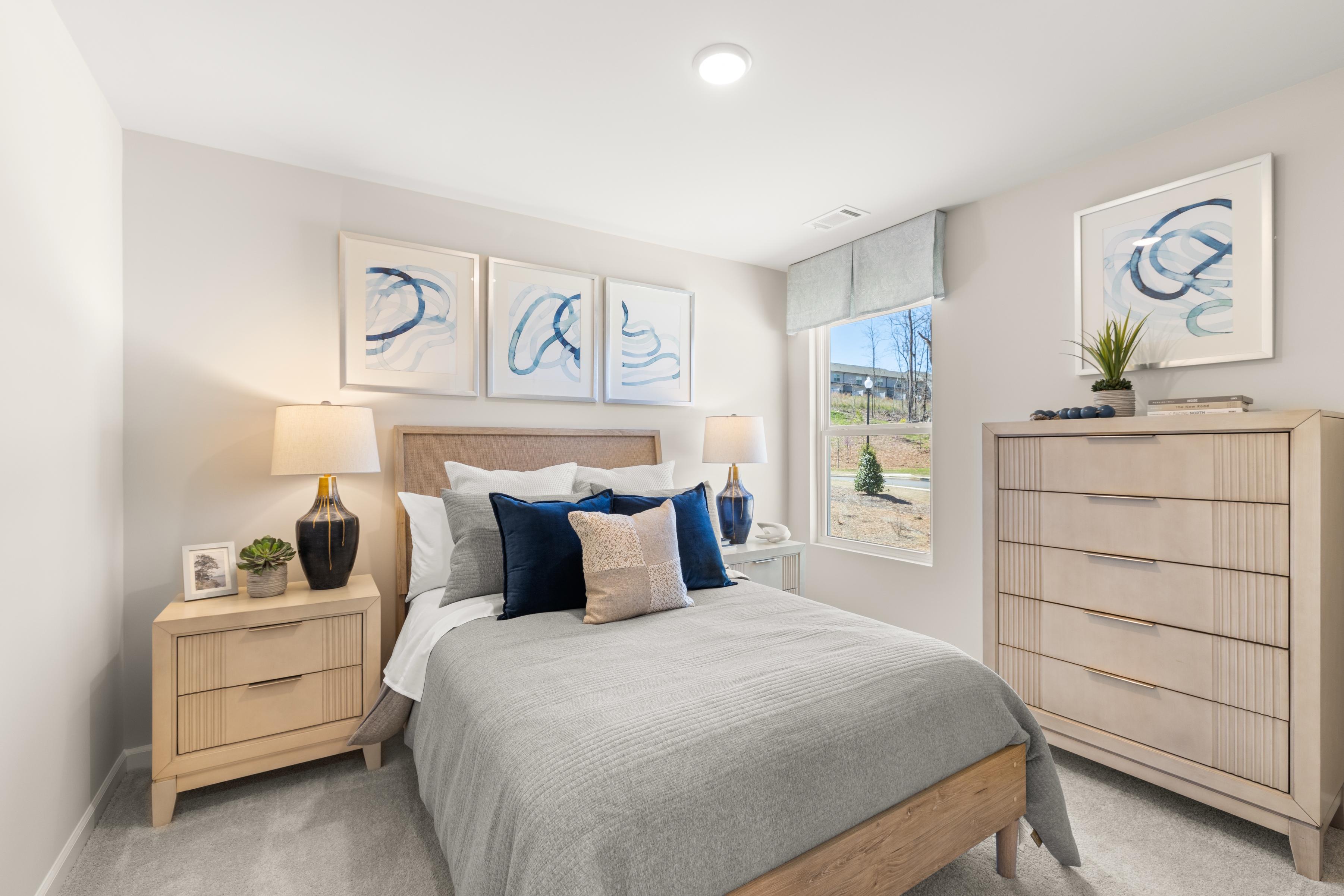 Cozy bedroom at The Bluffs in Canton, Georgia by Davidson Homes featuring gray queen bed, blue accents, wooden furniture, abstract art