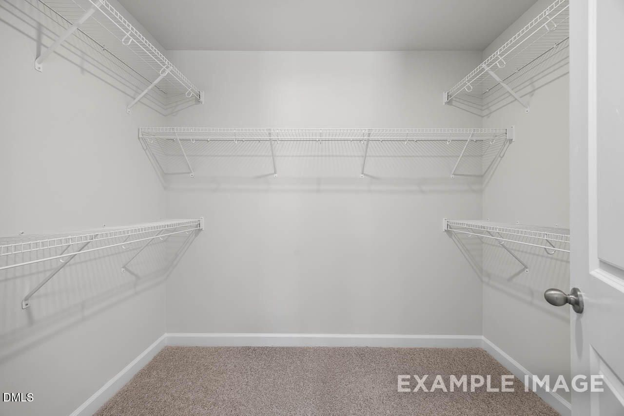 Spacious walk-in closet with white wire shelving and beige carpet in master suite of Davidson Homes The Adalynn A, Lillington, NC