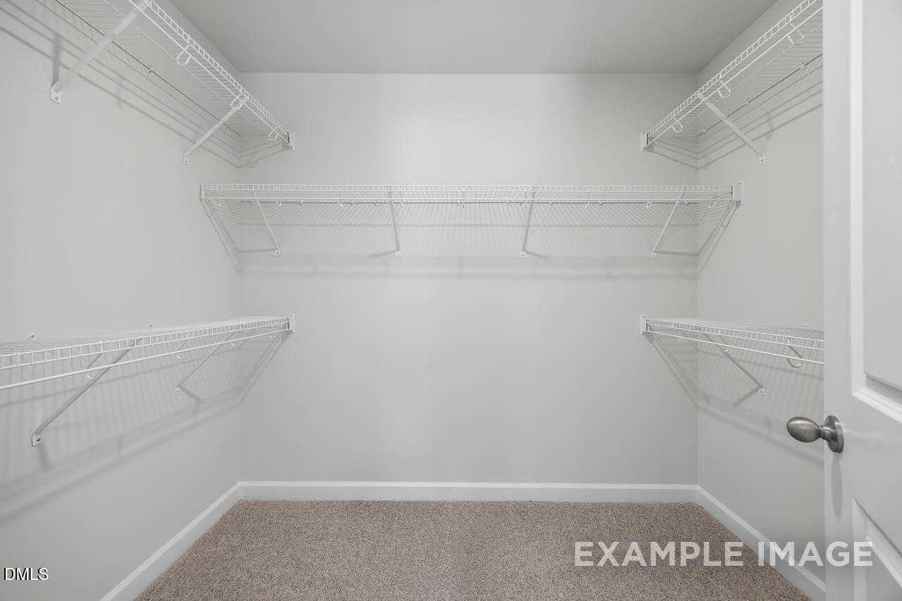Spacious walk-in closet with white wire shelving and beige carpet in master suite of Davidson Homes The Adalynn A, Lillington, NC