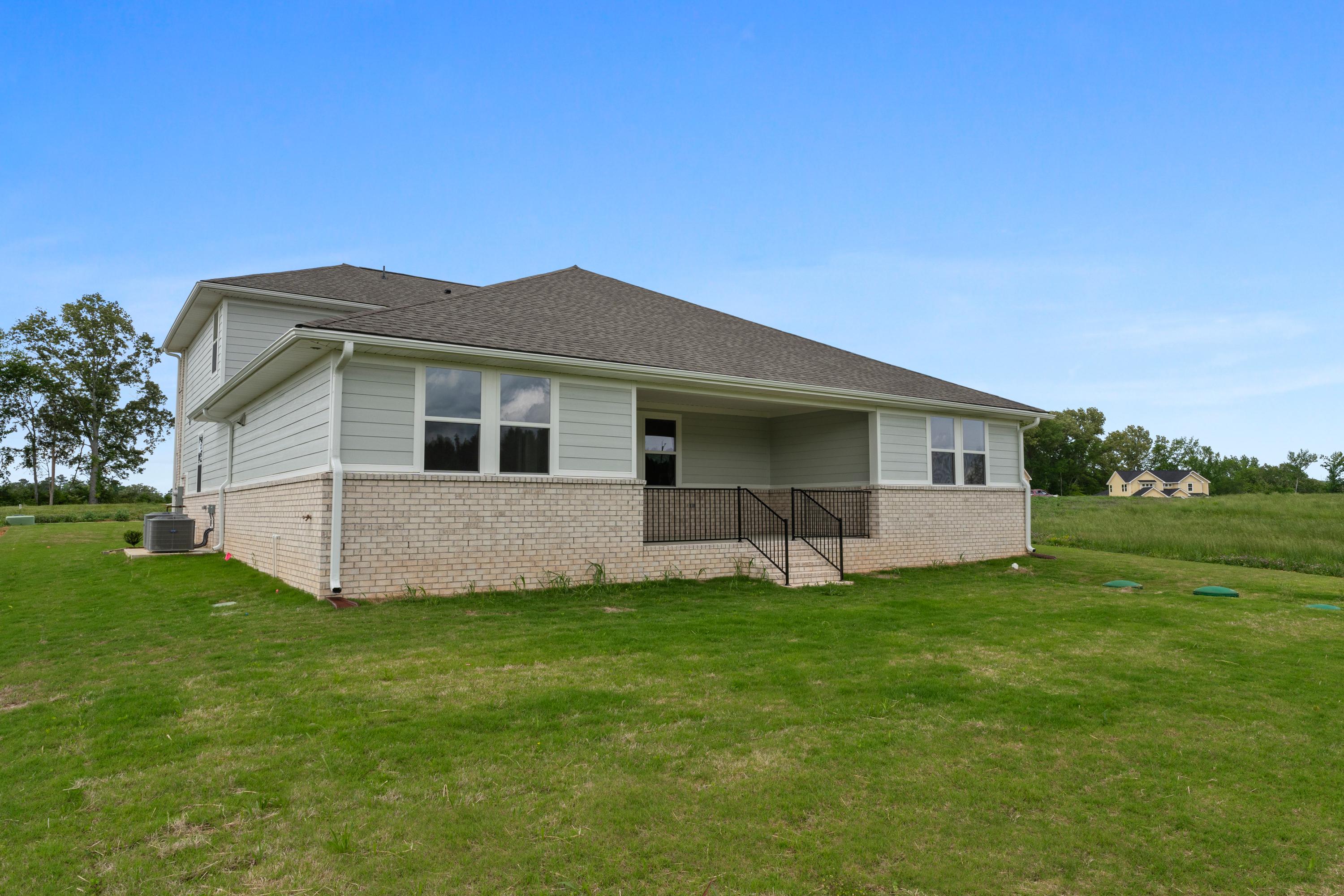Side elevation of The Haven E single-story home featuring gray siding, brick base, covered porch, and lush green yard