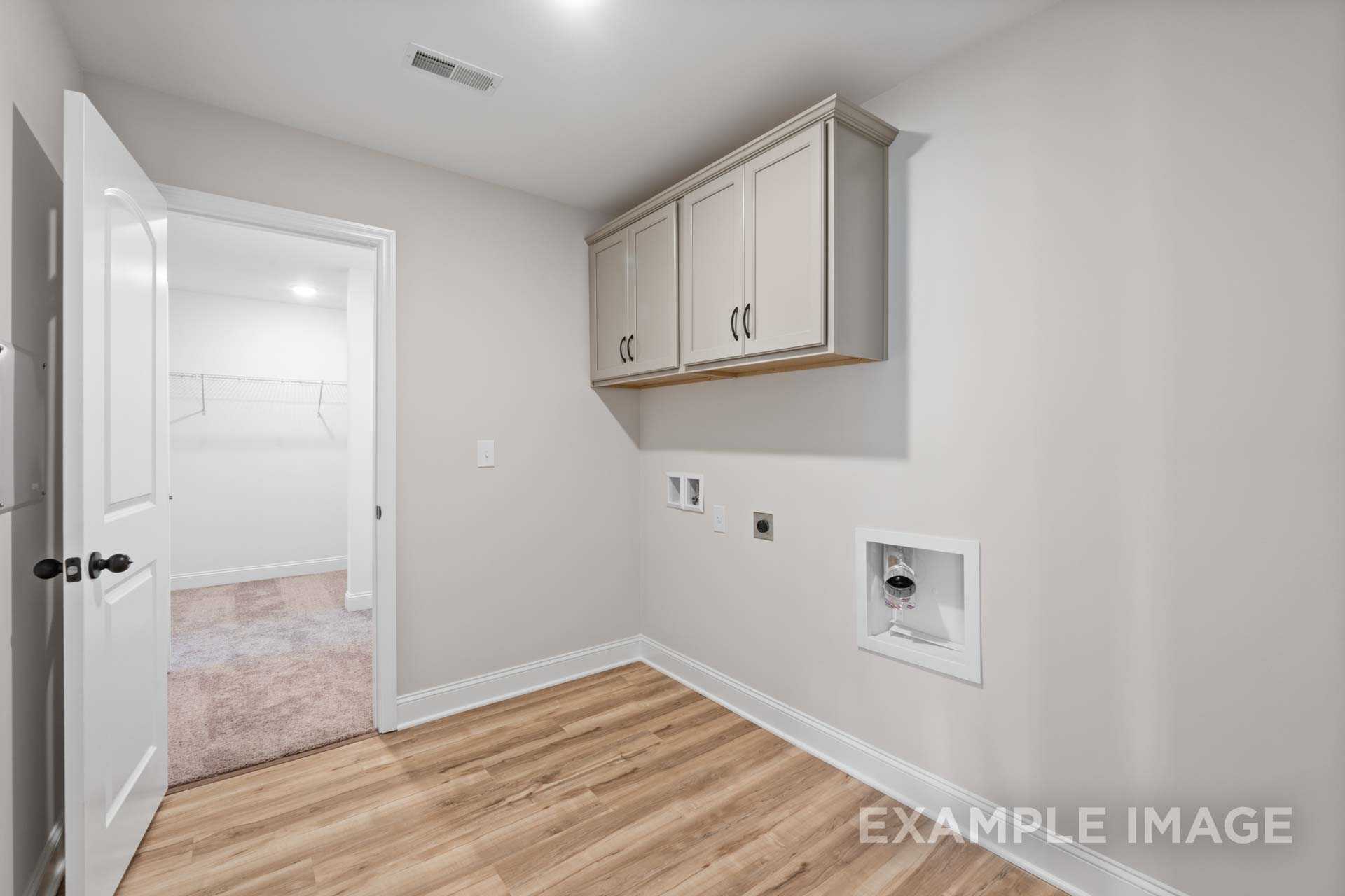 Spacious laundry room in The Holly M featuring cream upper cabinets, washer dryer hookups, utility sink, and adjacent walk-in closet