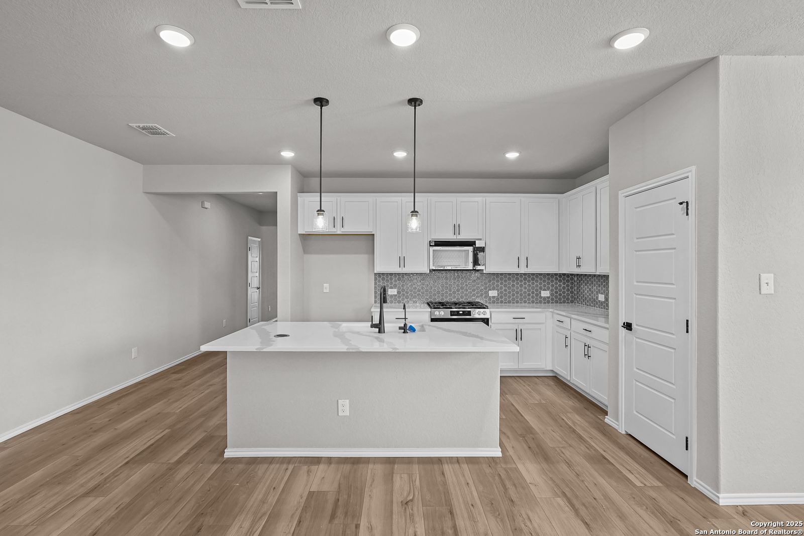 Modern white kitchen with quartz island, stainless appliances, subway tile backsplash in The Daphne K 4-bedroom home, San Antonio TX