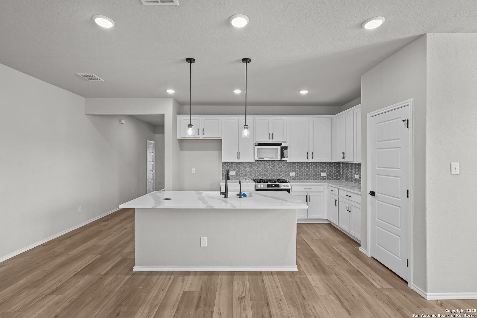 Modern white kitchen with quartz island, stainless appliances, subway tile backsplash in The Daphne K 4-bedroom home, San Antonio TX