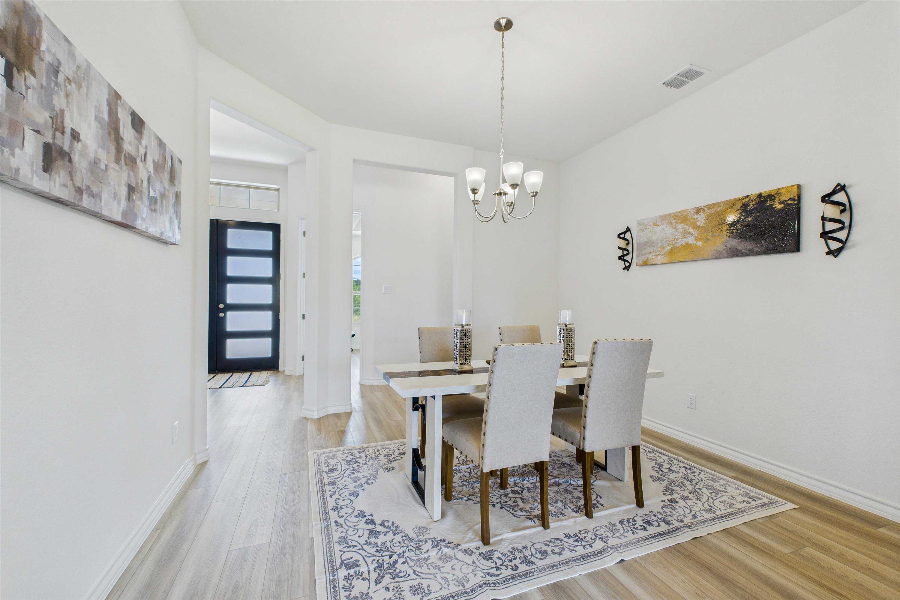 Elegant dining room with wooden table, upholstered chairs, chandelier, and abstract art in The Summerlin C 4-bedroom home, Castroville, Texas