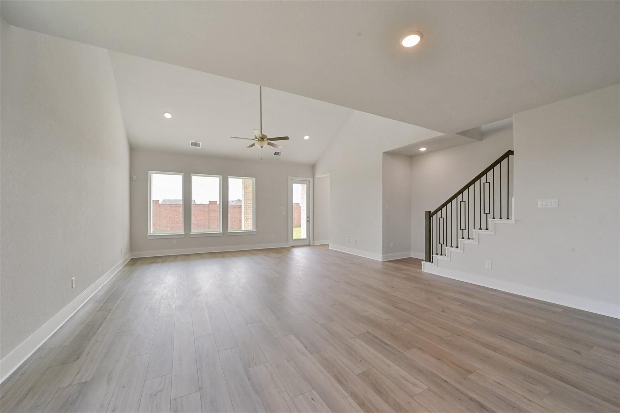 Spacious two-story entryway with light hardwood floors, large windows, ceiling fan, and wrought iron staircase in Davidson Homes The Zion A, Lago Mar, Texas City