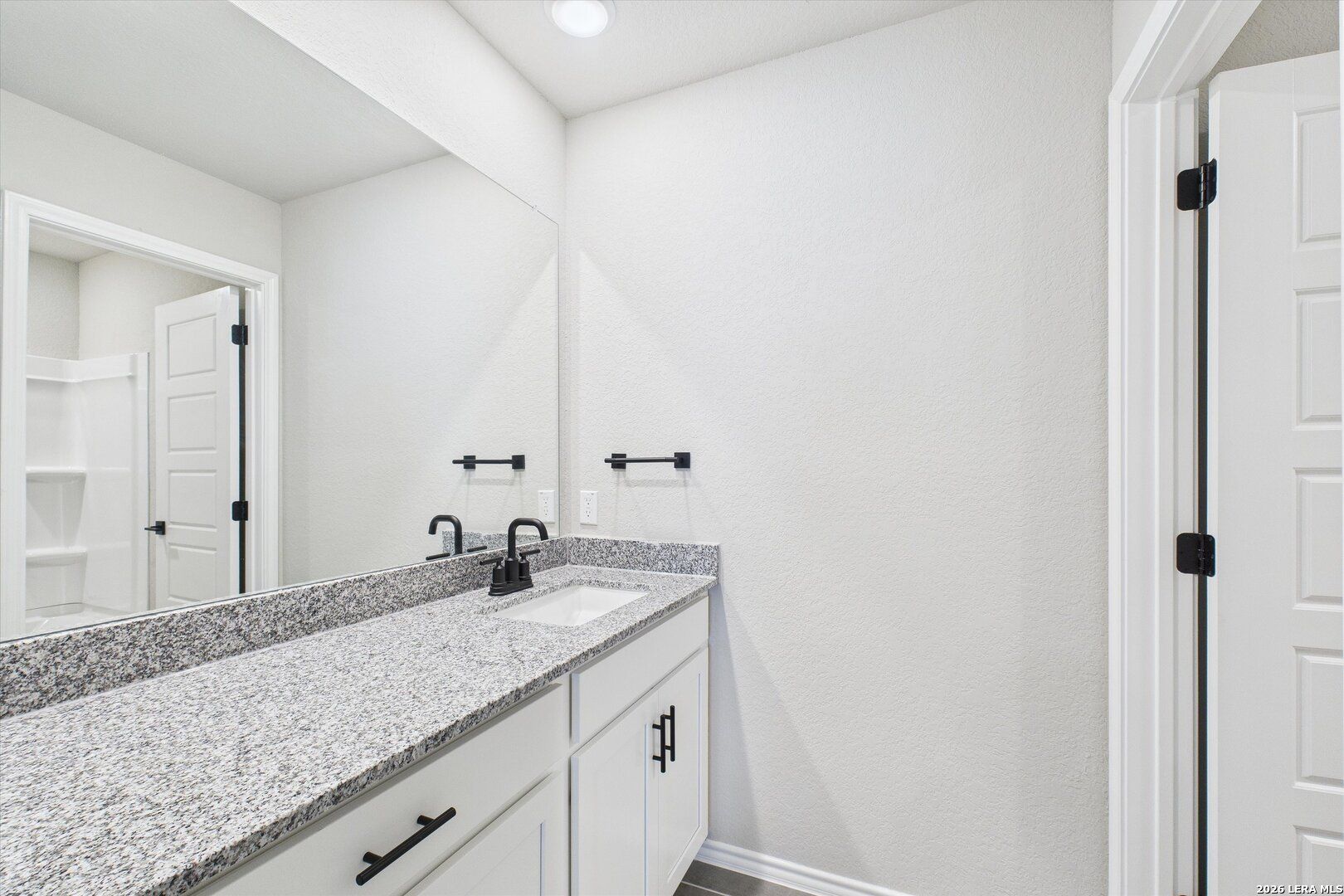 Modern master bathroom double vanity with granite countertop, white cabinets, and large mirror in Davidson Homes The Charlotte A, San Antonio