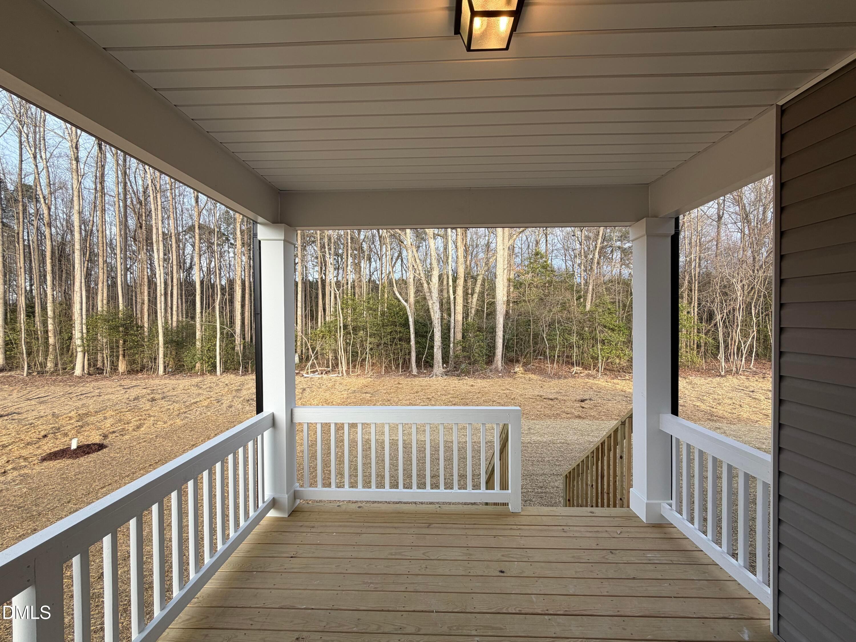 Covered back porch with white railings, wooden deck, and lantern light overlooking wooded yard in The Ash B home, Lillington, NC