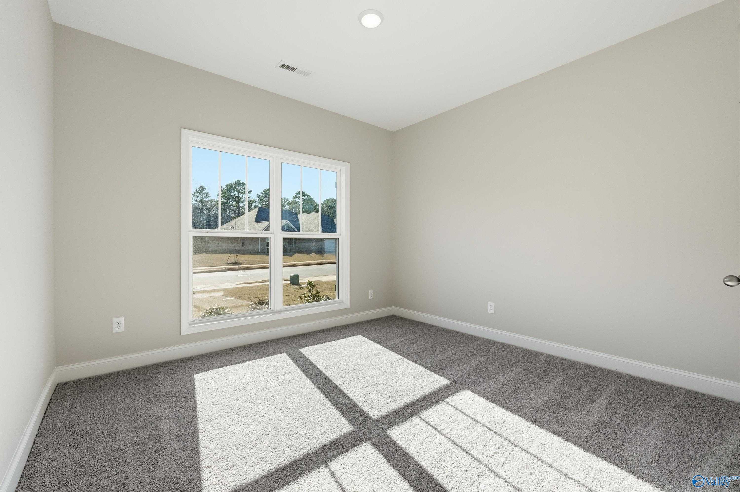 Bright secondary bedroom with beige walls, gray carpet, and large window overlooking trees in Davidson Homes The Everett, Creekside, Harvest, Alabama