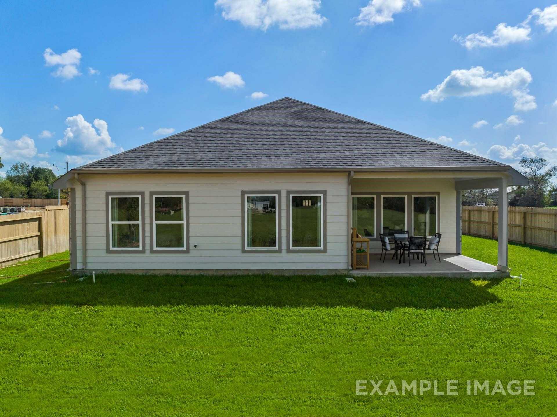 Back view of The Acadia A 4-bedroom home featuring covered patio, large windows, and fenced green yard in Lago Mar, Texas City, Texas