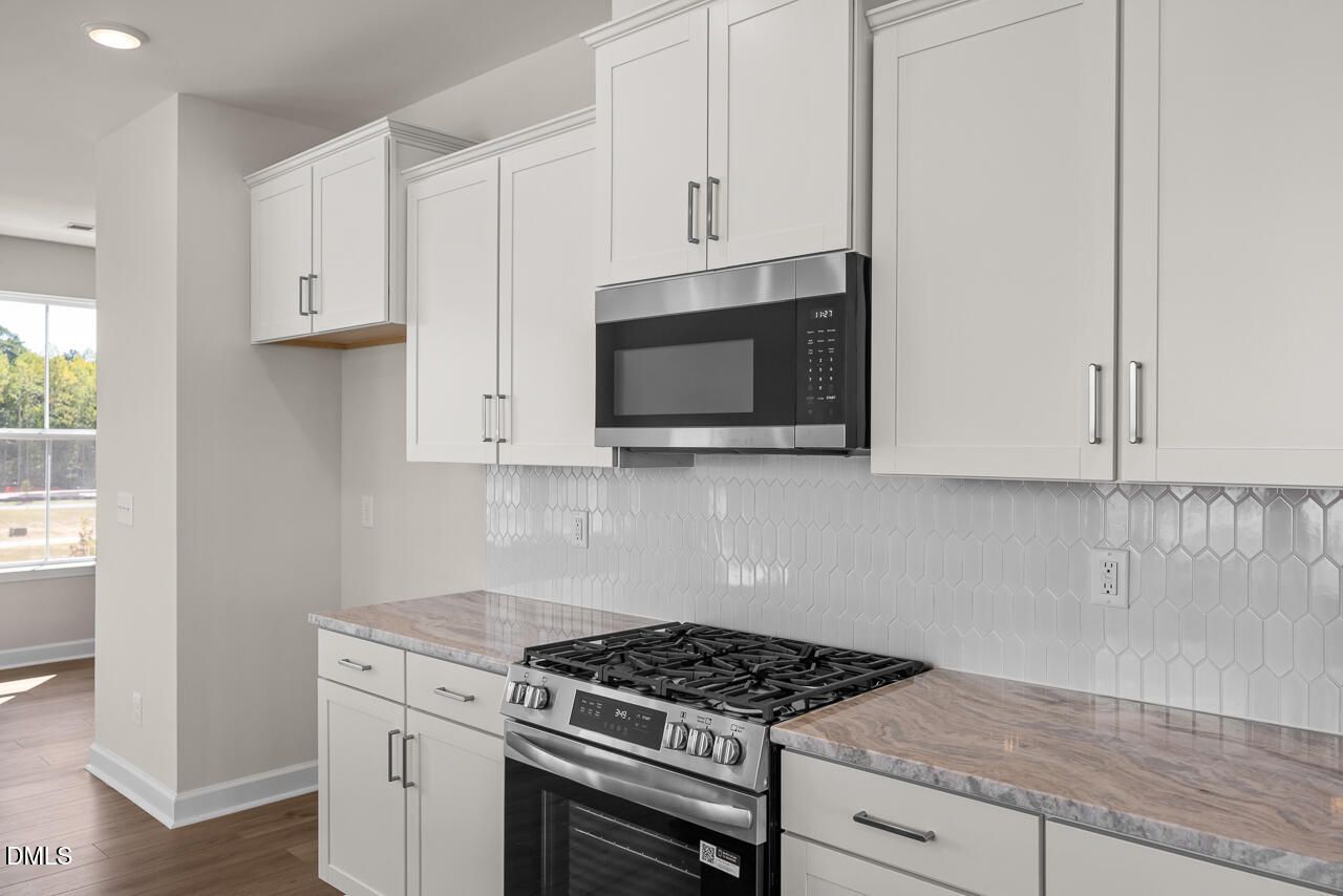 Modern kitchen with white shaker cabinets, gas range, stainless microwave, and hexagon tile backsplash in Davidson Homes' The Mitchell, Knightdale NC