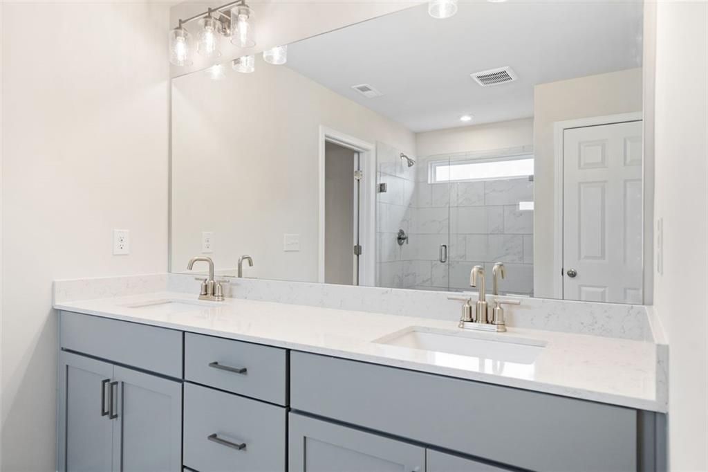 Modern master bathroom double vanity with white quartz counters, gray cabinets, and frameless shower in The Willow D home, Hoschton, GA