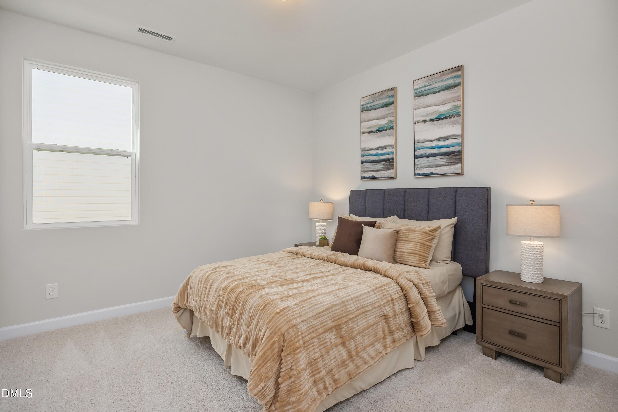 Serene secondary bedroom with beige bedding, tufted headboard, lamps, abstract art, and large window in Davidson Homes The Preston C, Lillington, NC